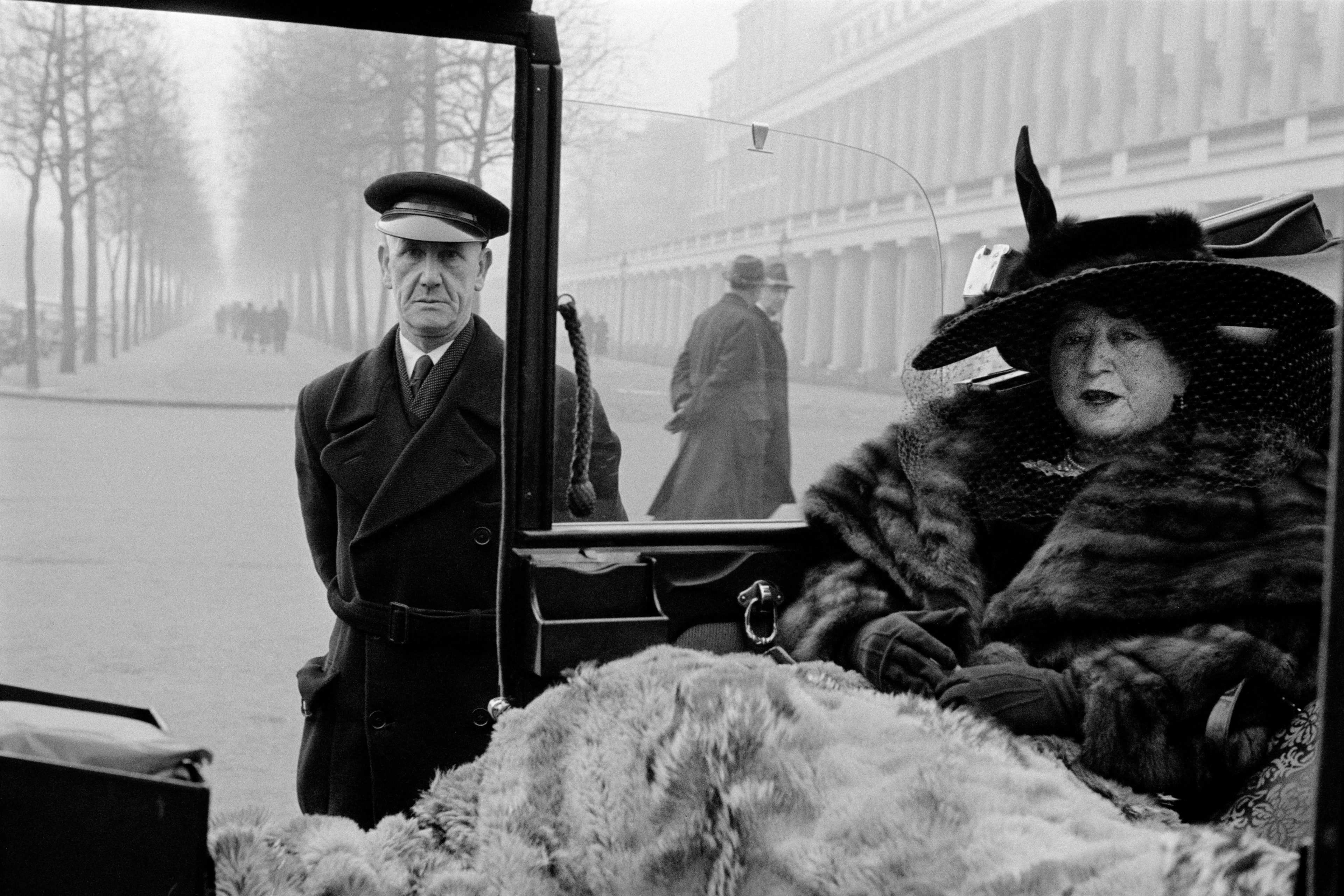 Imagen en blanco y negro, mujer con abrigo de piel sentada en un coche descapotable