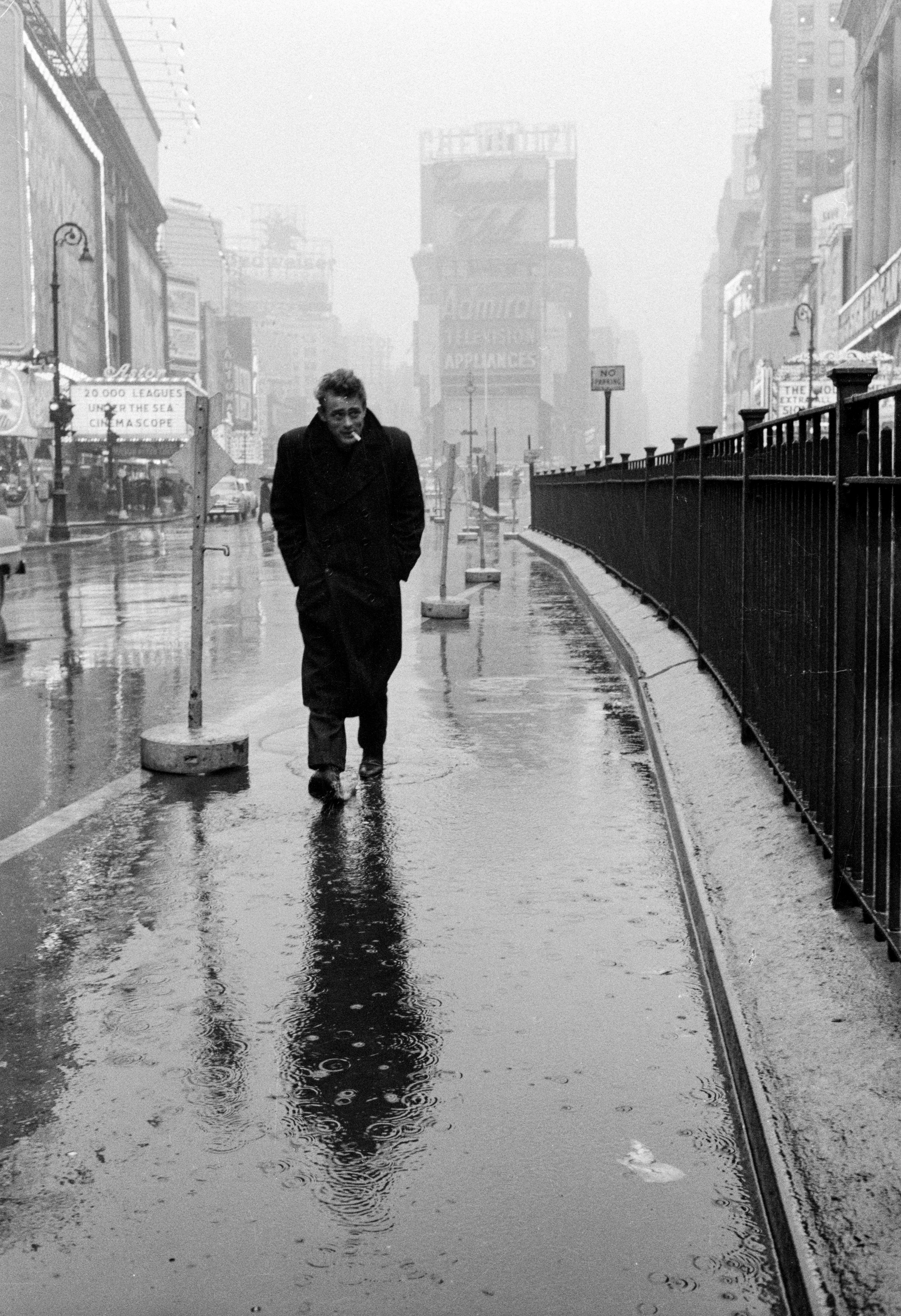 Imagen en blanco y negro, James Dean camina bajo la lluvia con un cigarro en la boca por Times Square