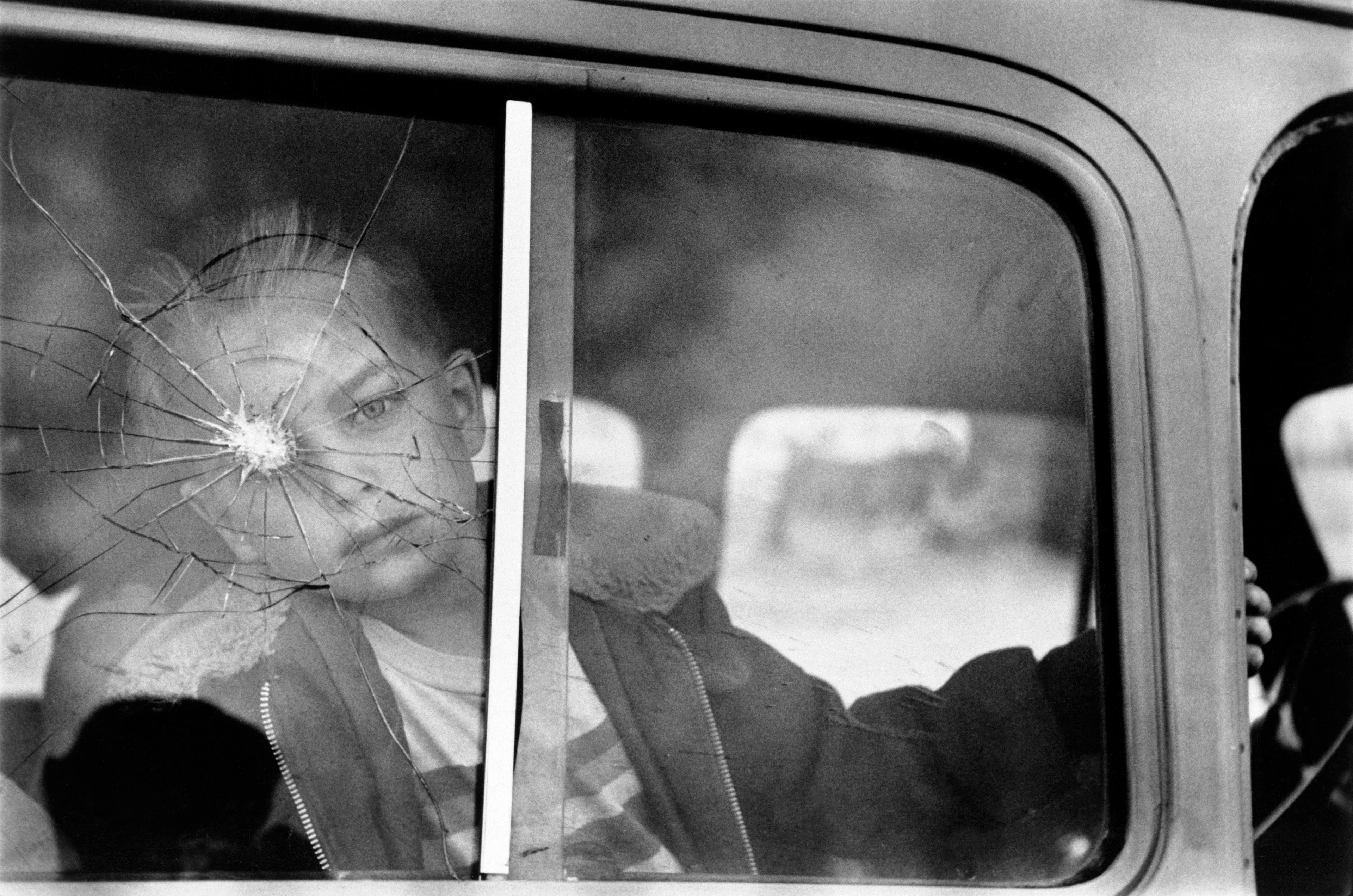 Imagen en blanco y negro, un niño mira a través de una ventanilla de coche rota