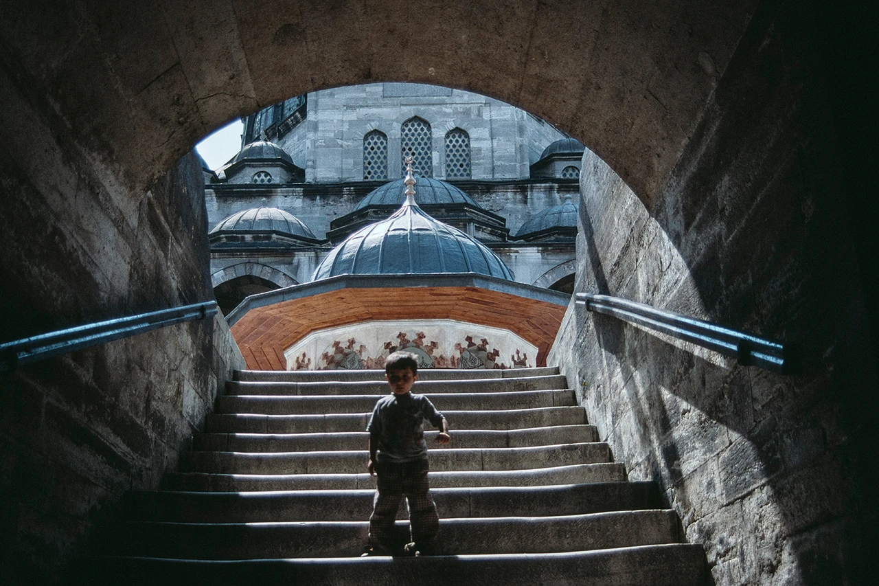 Un niño baja corriendo las escaleras, al fondo se ve un edificio turco