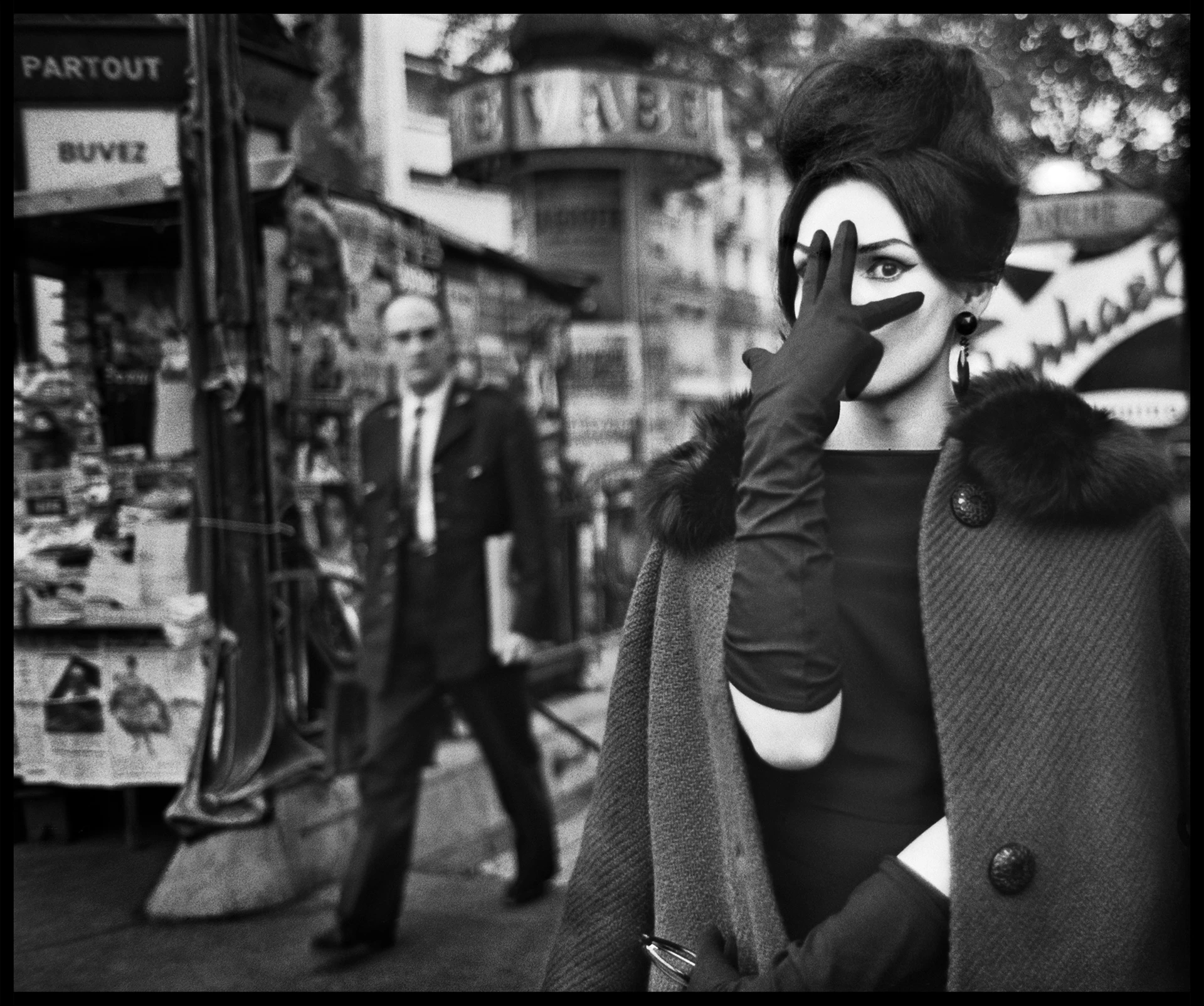 Black-and-white image, iconic image of an elegant lady with a pinned-up hairstyle and elbow-length gloves; she holds her right hand with her fingers spread across her face