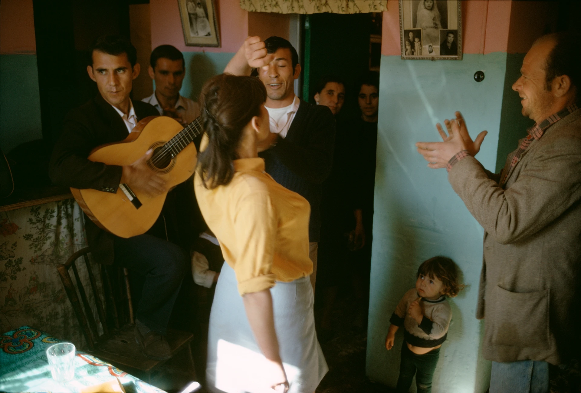 Gente toca música y baila alegremente en una habitación, paredes de colores, un niño pequeño mira con asombro