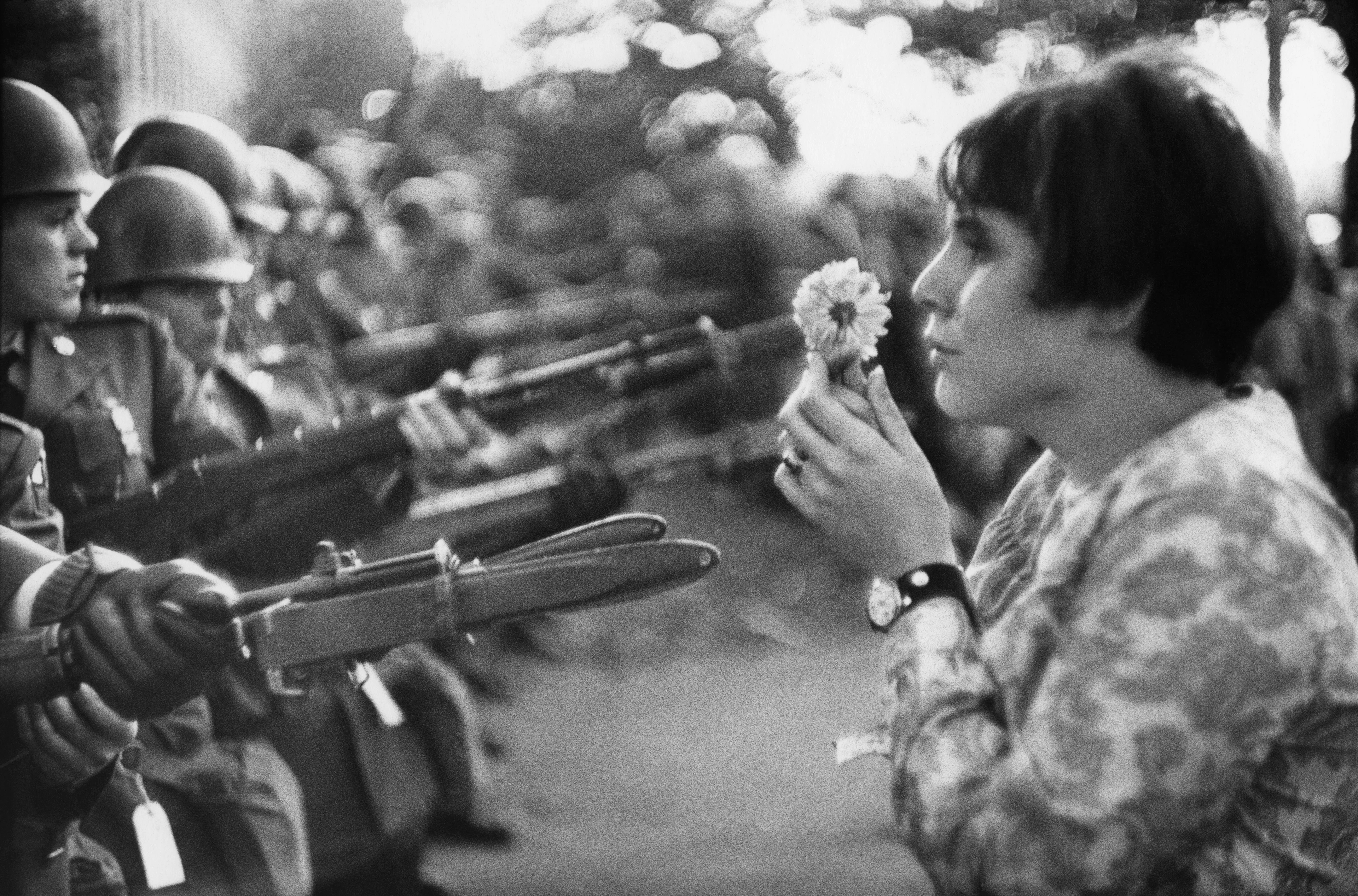 Black-and-white image, woman confronts soldiers wielding weapons with a flower