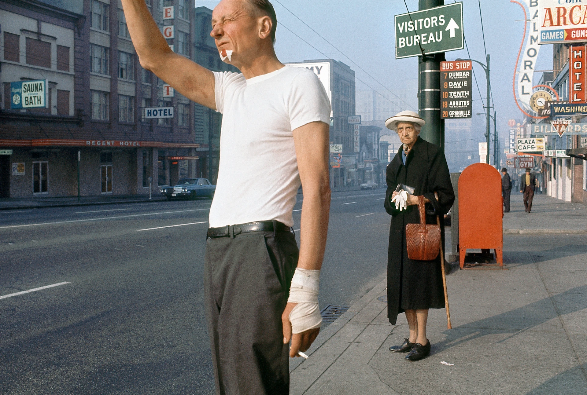 Man with a cigarette and injuries to his face and hand stands on the street and seems to be hailing a taxi