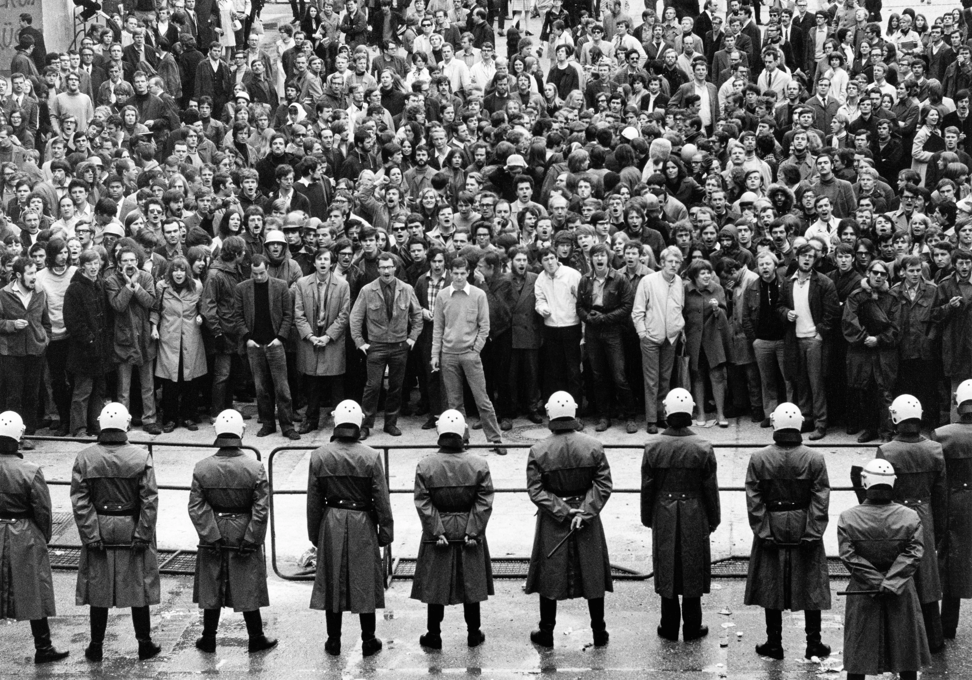 Imagen en blanco y negro, manifestantes y policías se enfrentan en un bloqueo