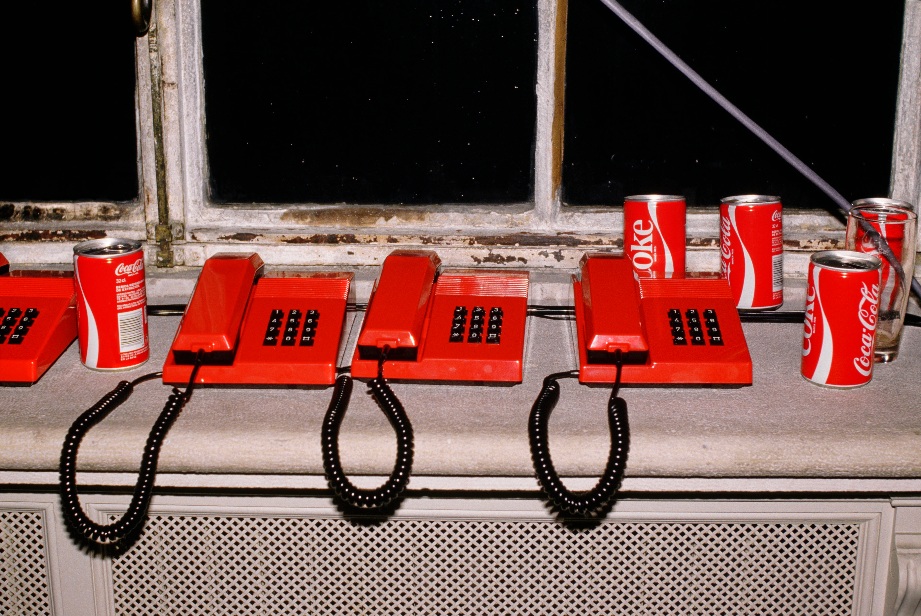Telefoni con filo rossi e lattine di Coca Cola su un davanzale grigio.
