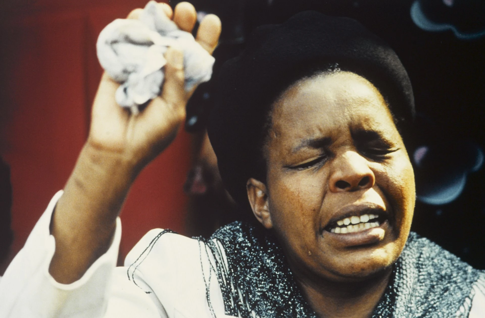 Donna di colore con gli occhi chiusi e un’espressione stravolta tiene in mano in alto un fazzoletto.