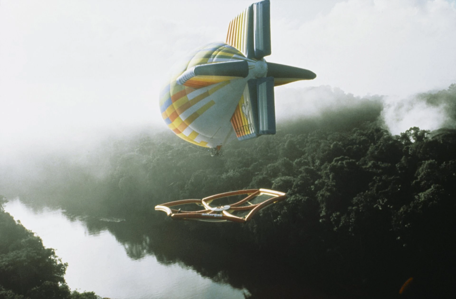 A research platform of nets and inflatable structures, suspended from a colourful zeppelin, glides above a river stretch of the Amazon rainforest.