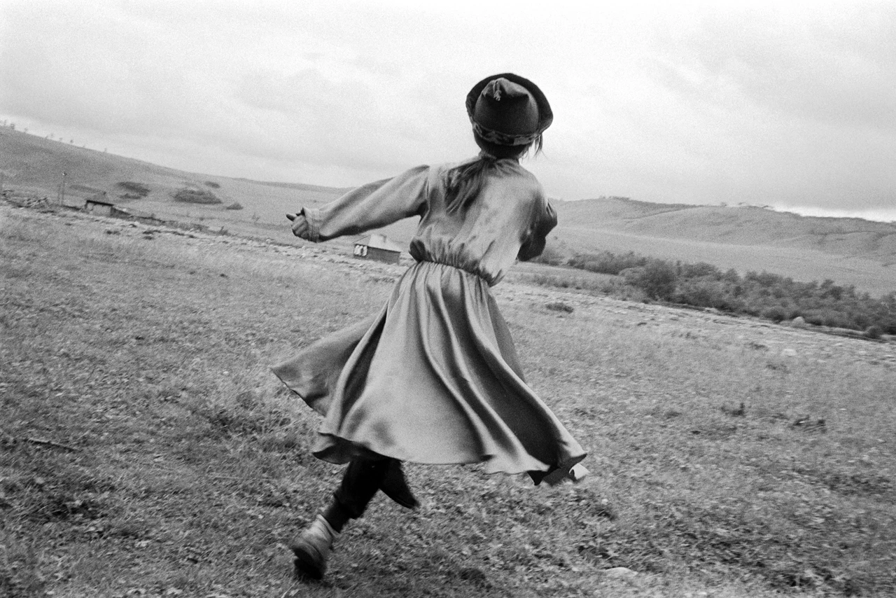 Black and white image of a nomad girl in a long dress skipping across a meadow in the barren Siberian landscape.