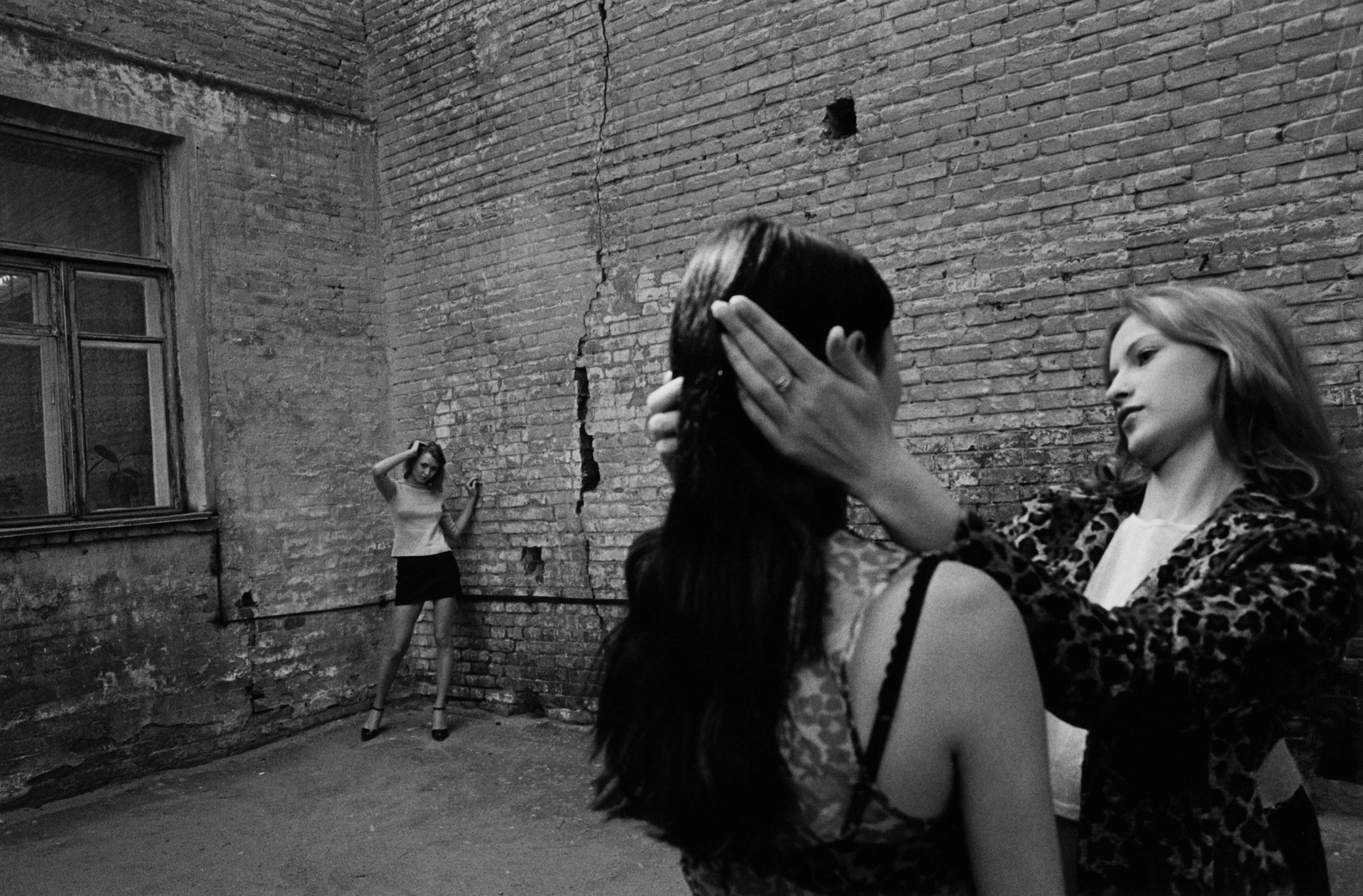 黑白照片，三位衣著單薄的俄羅斯女子在後院中，其中一人正托著另一人的頭。