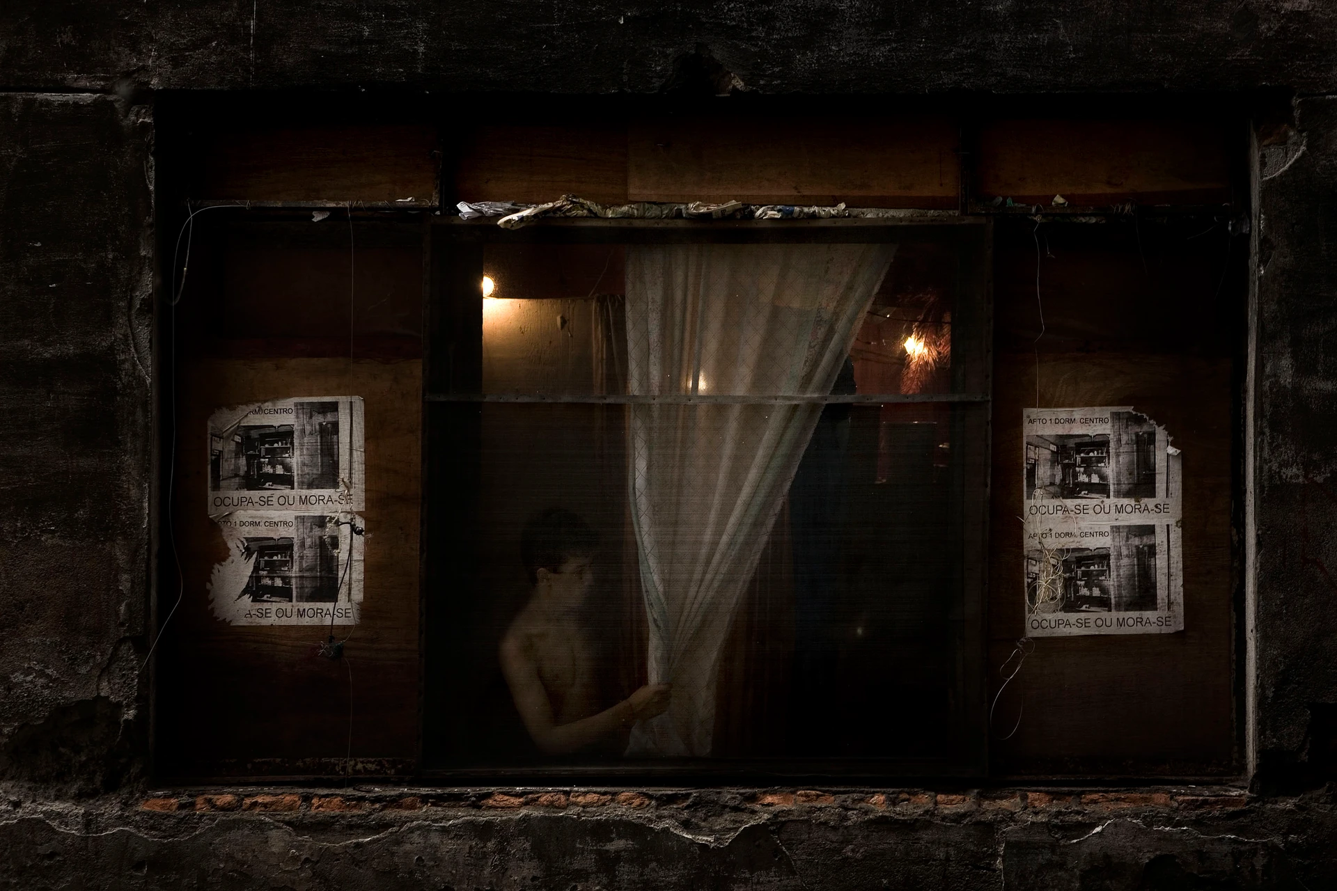 試拍，聖保羅一扇邊上被木板封死的窗戶，中間有一名年輕男子在鐵絲後，手中拿著窗簾。