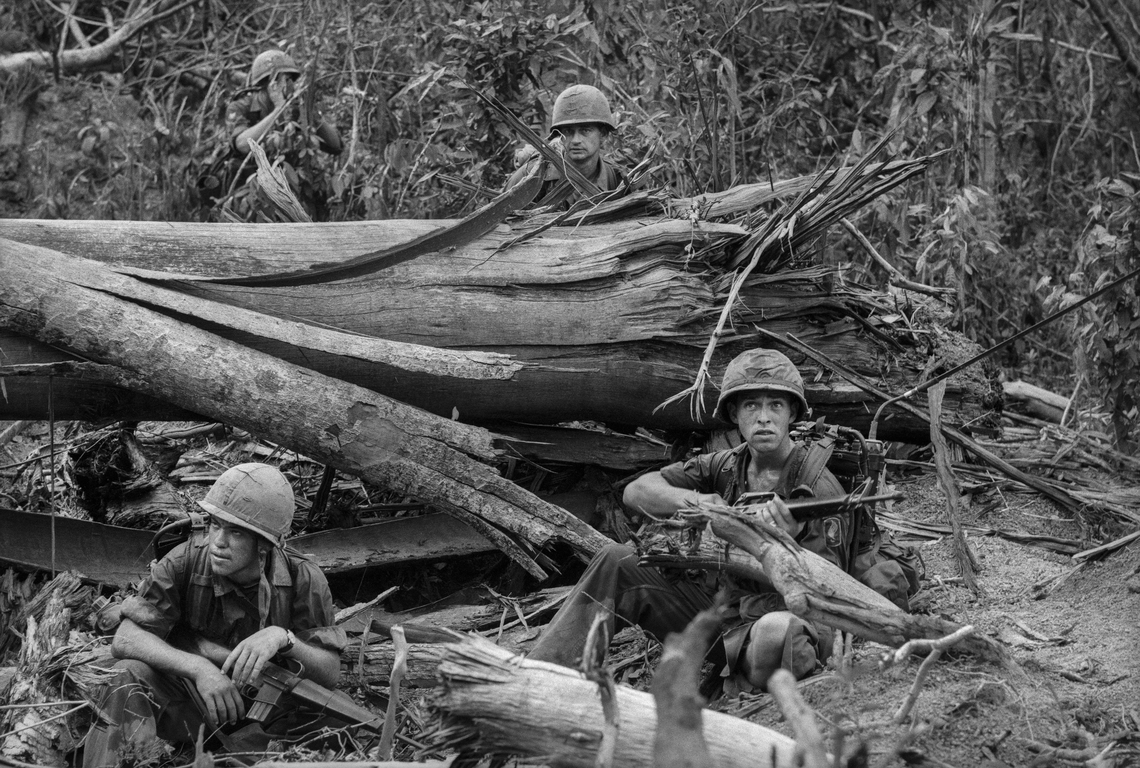 Motyw czarno-biały, wojna w Wietnamie, żołnierze czają się przy wielkim, rozdrobnionym pniu drzewa