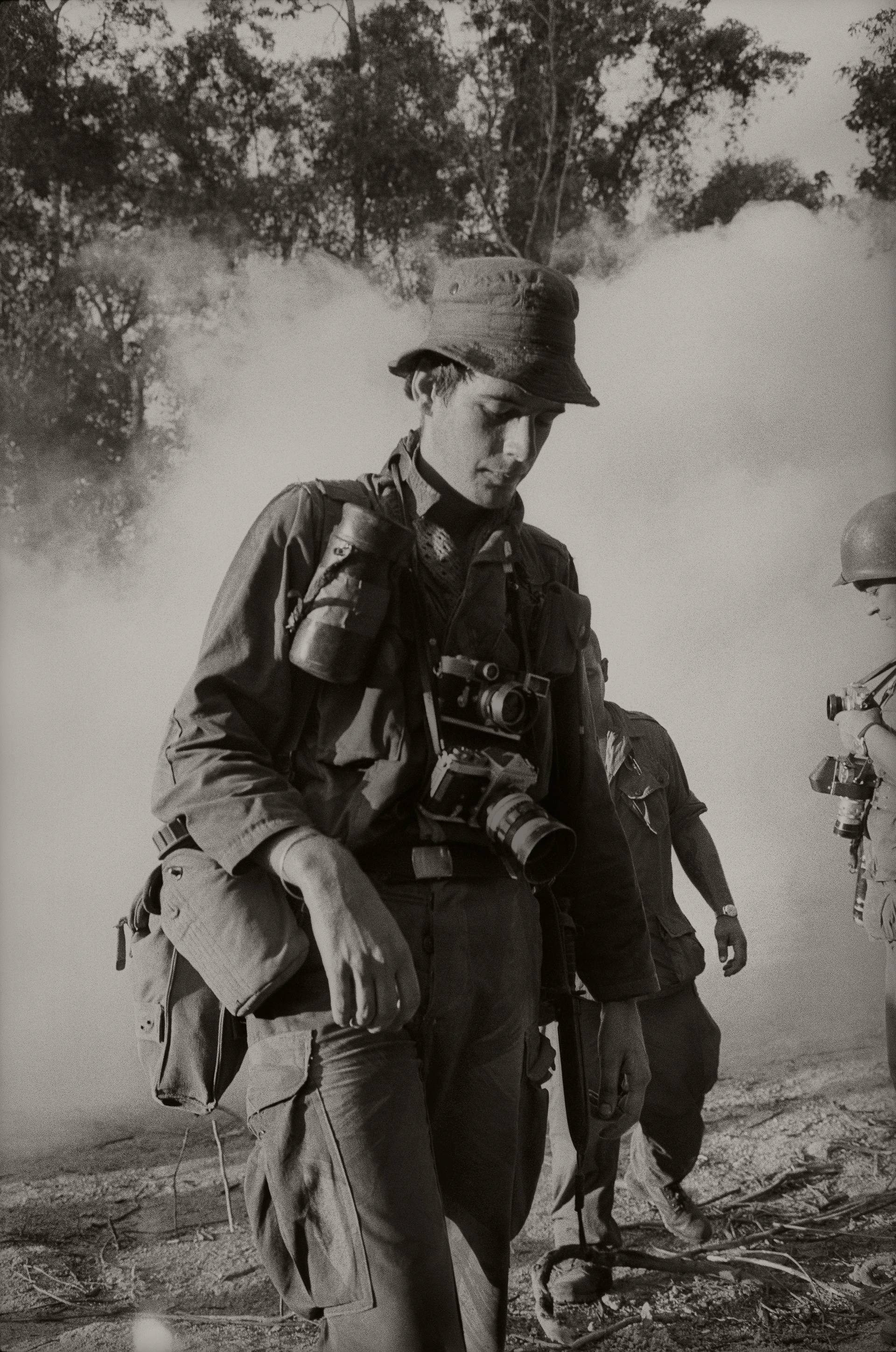 Czarno-biały portret Tima Page'a podczas wojny w Wietnamie, obładowanego sprzętem fotograficznym