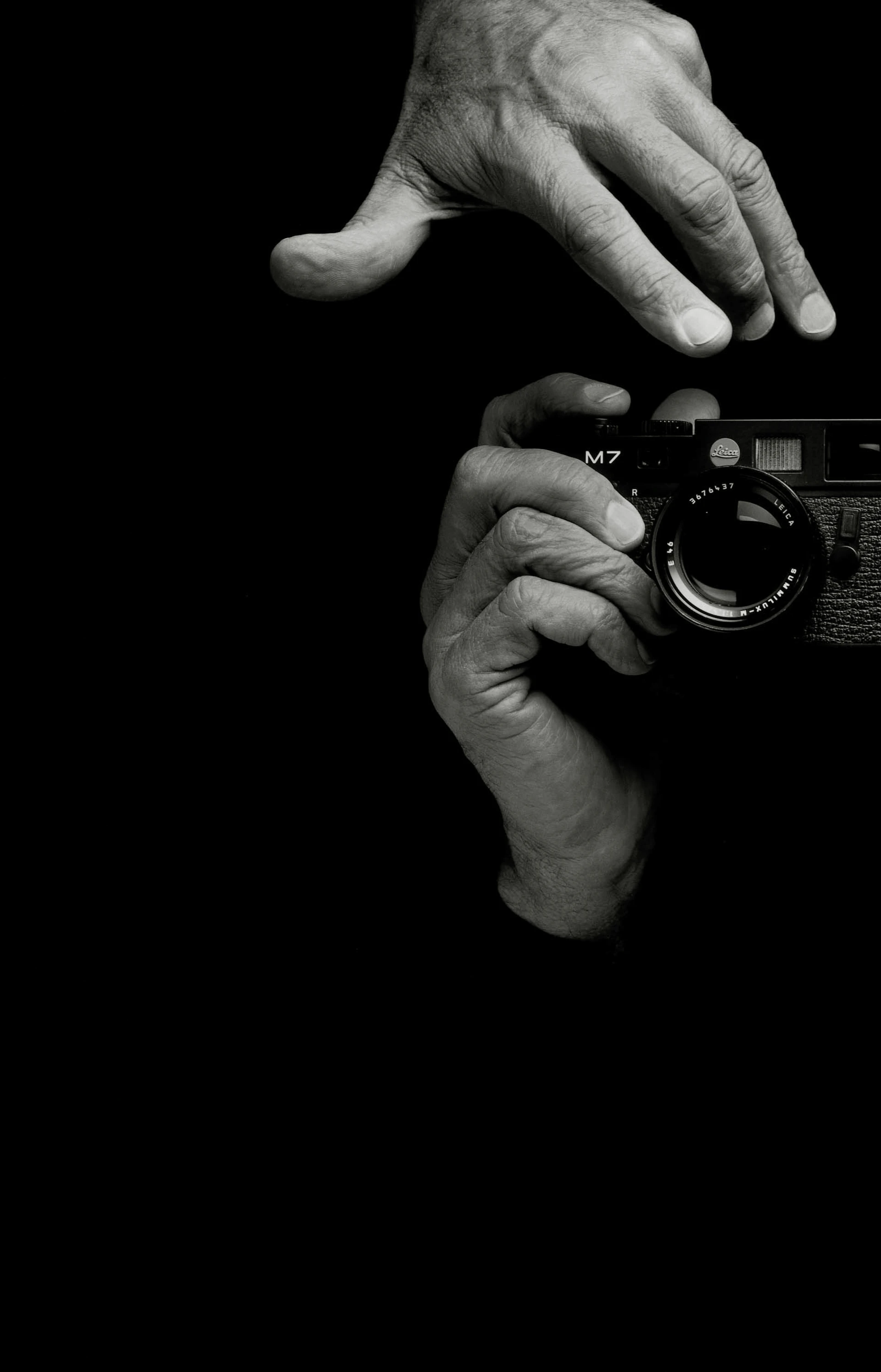 Annuncio pubblicitario stampato in bianco e nero con il logo, un breve testo e, come unico soggetto, due mani che azionano una fotocamera Leica M7.