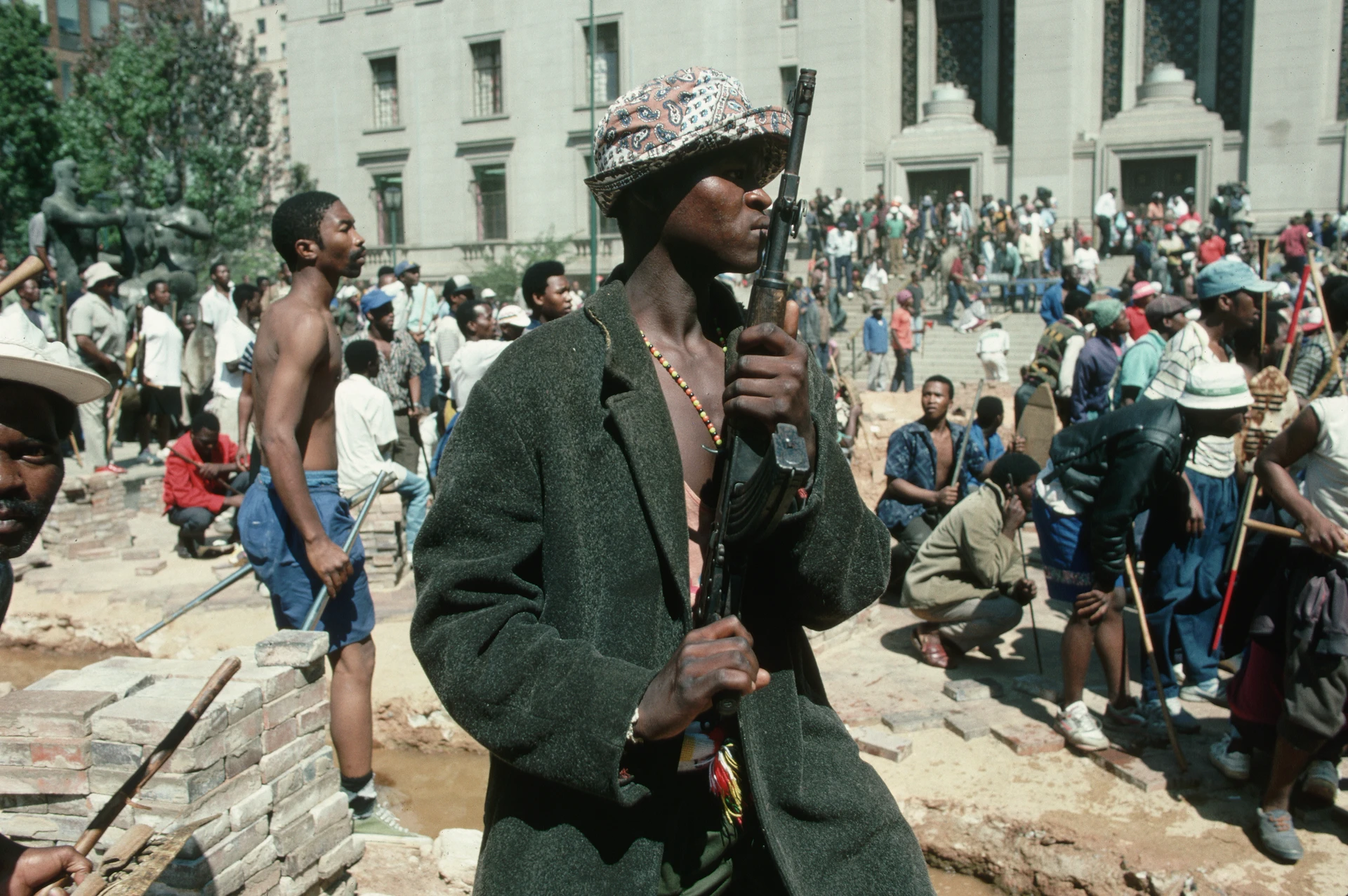 Una protesta di massa di persone di colore sudafricane che per strada, armate di bastoni e fucili, guardano in una direzione, pronti per l’escalation della protesta.