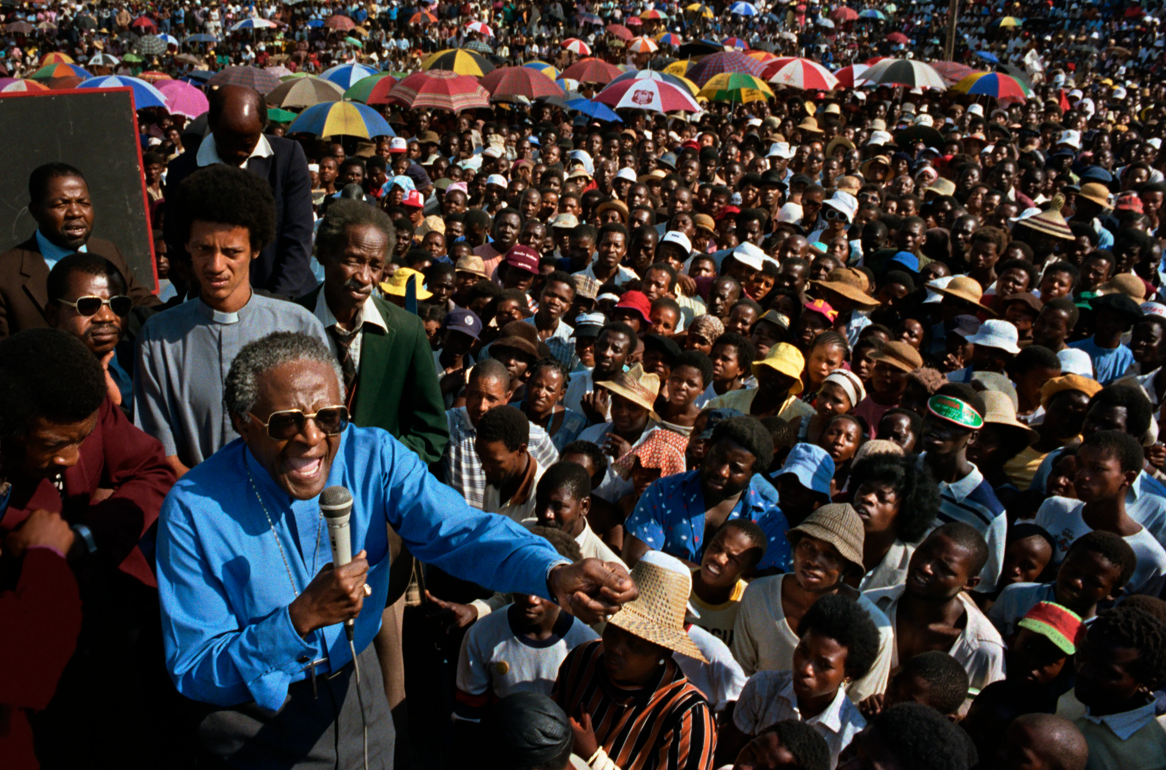 L’arcivescovo Desmond Tutu in una giornata soleggiata parla con vigore durante una manifestazione davanti a una folla di sudafricani di colore che lo ascoltano rapiti.