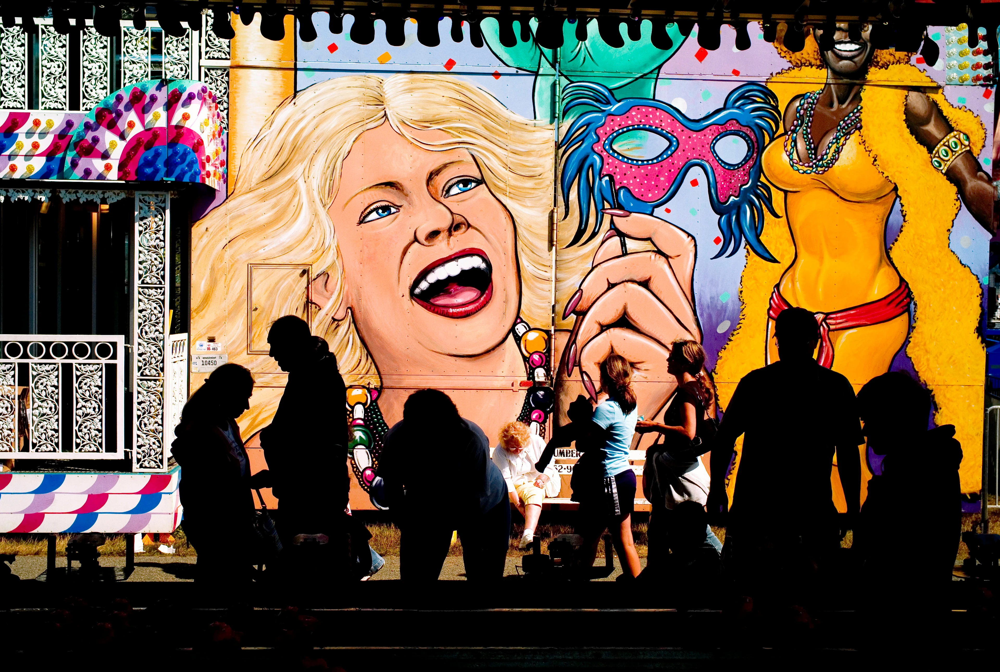 Ein typisch buntes Wandgemälde in einem Freizeitpark mit Besuchern davor, teilweise in Schattensilhouette.