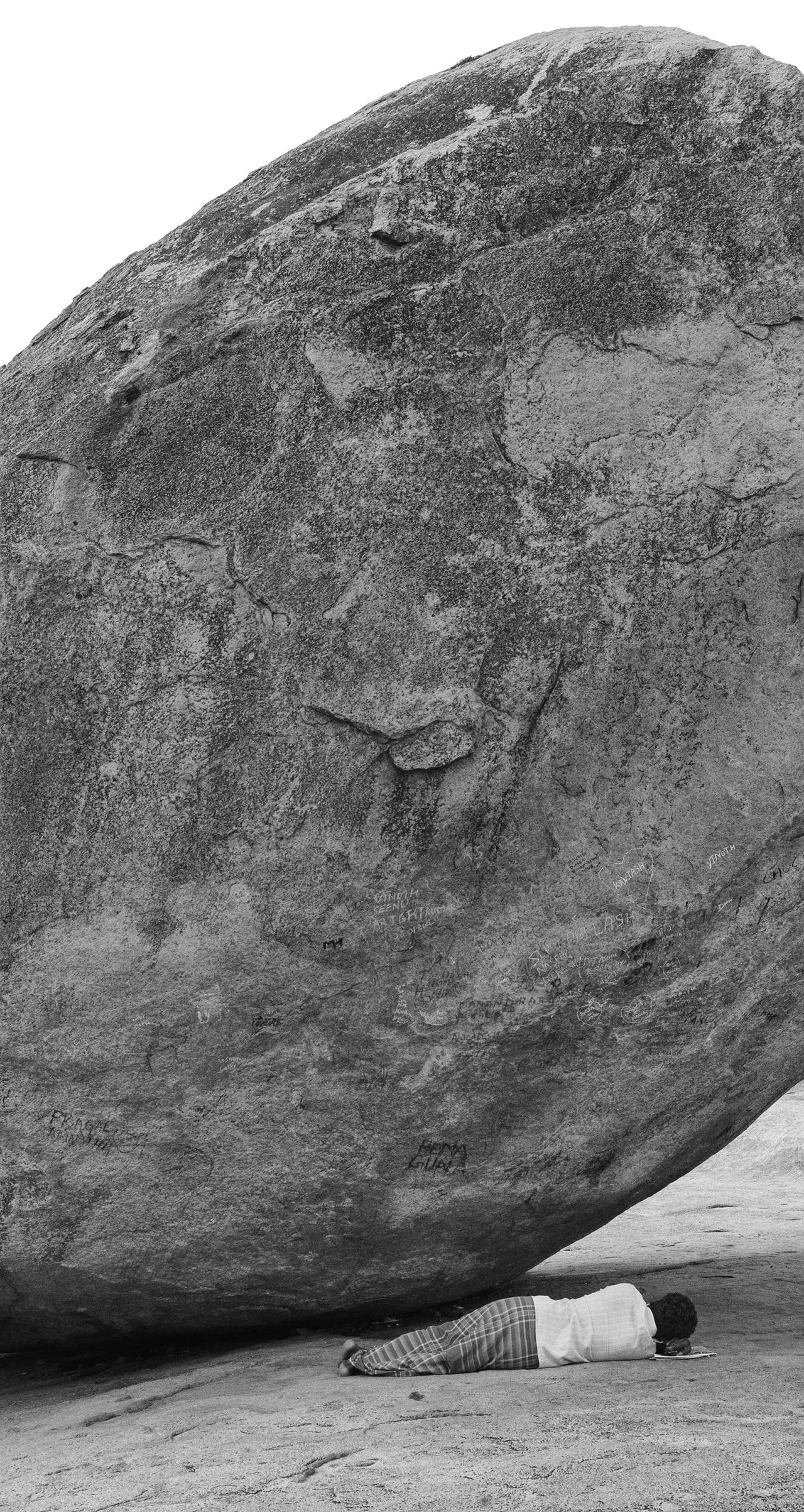 黑白照片:一块大而圆的岩石斜倚在露天岩面上,一个相对矮小的人躺在岩石的阴影下睡觉。