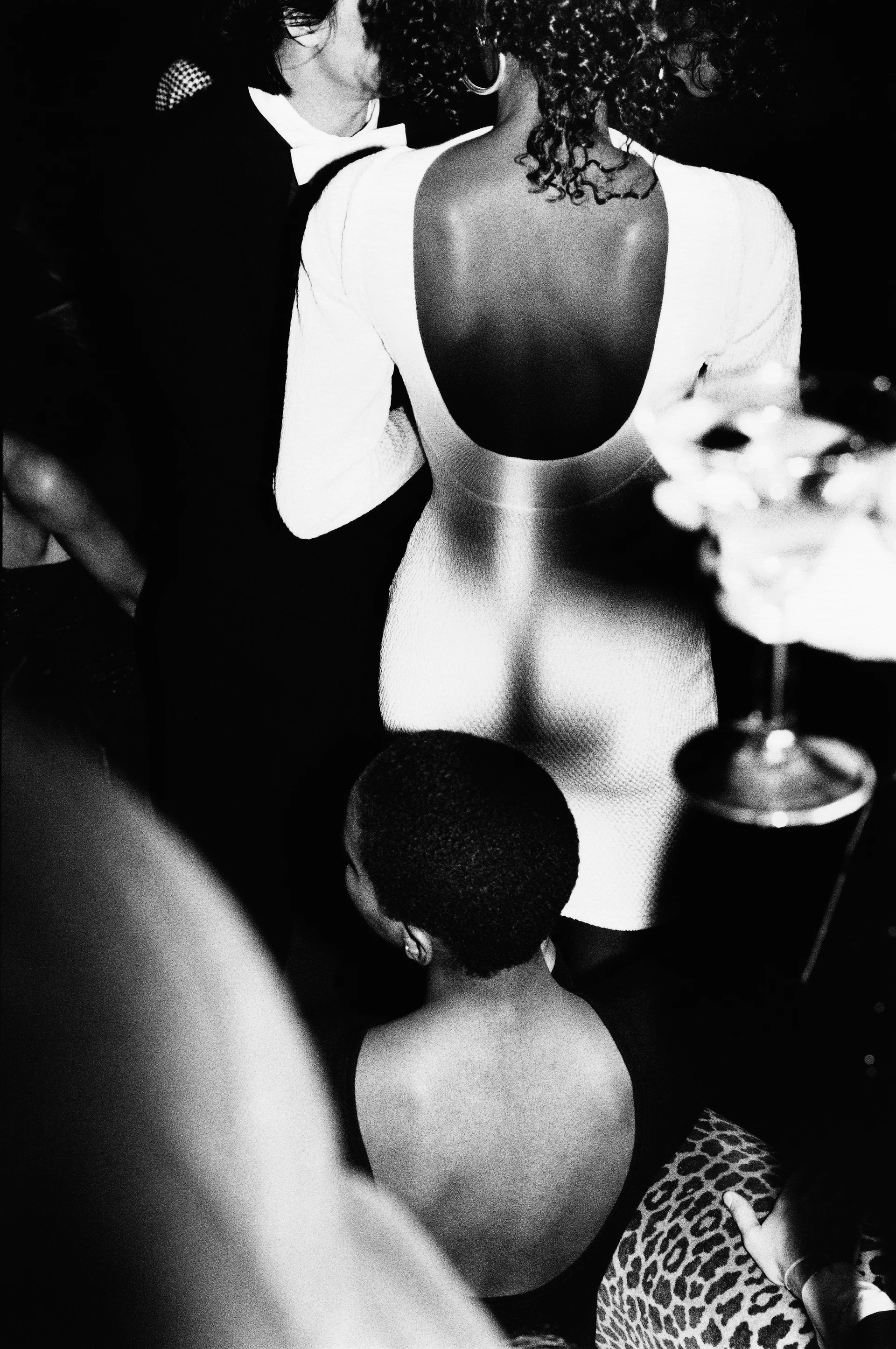 Fotografía en blanco y negro que muestra el ajetreo de un cóctel con modelos con elegantes vestidos.