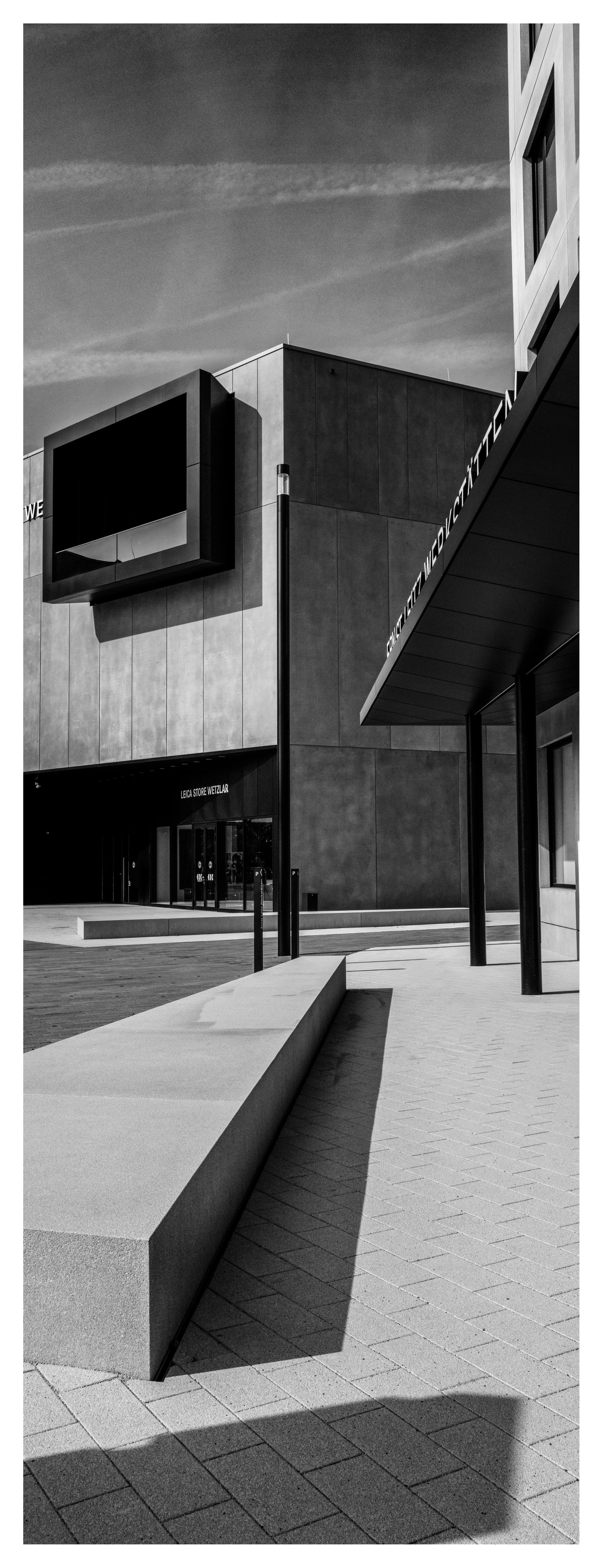 黑白照片:现代建筑群的外观,强烈的阳光照射在清晰的线条、敞亮的窗户和宽阔的混凝土表面上。