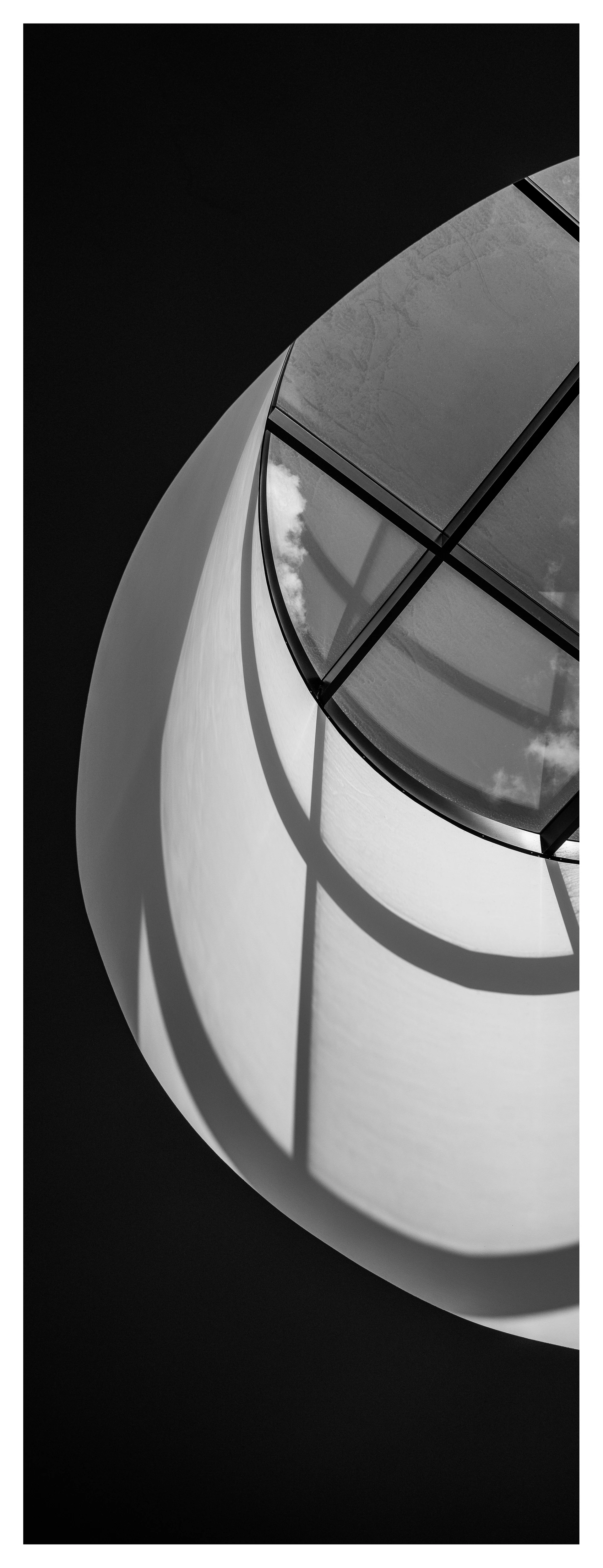 黑白照片:一个带横梁的圆形天窗将柔和的阴影和光弧投射到弯曲的内墙上。