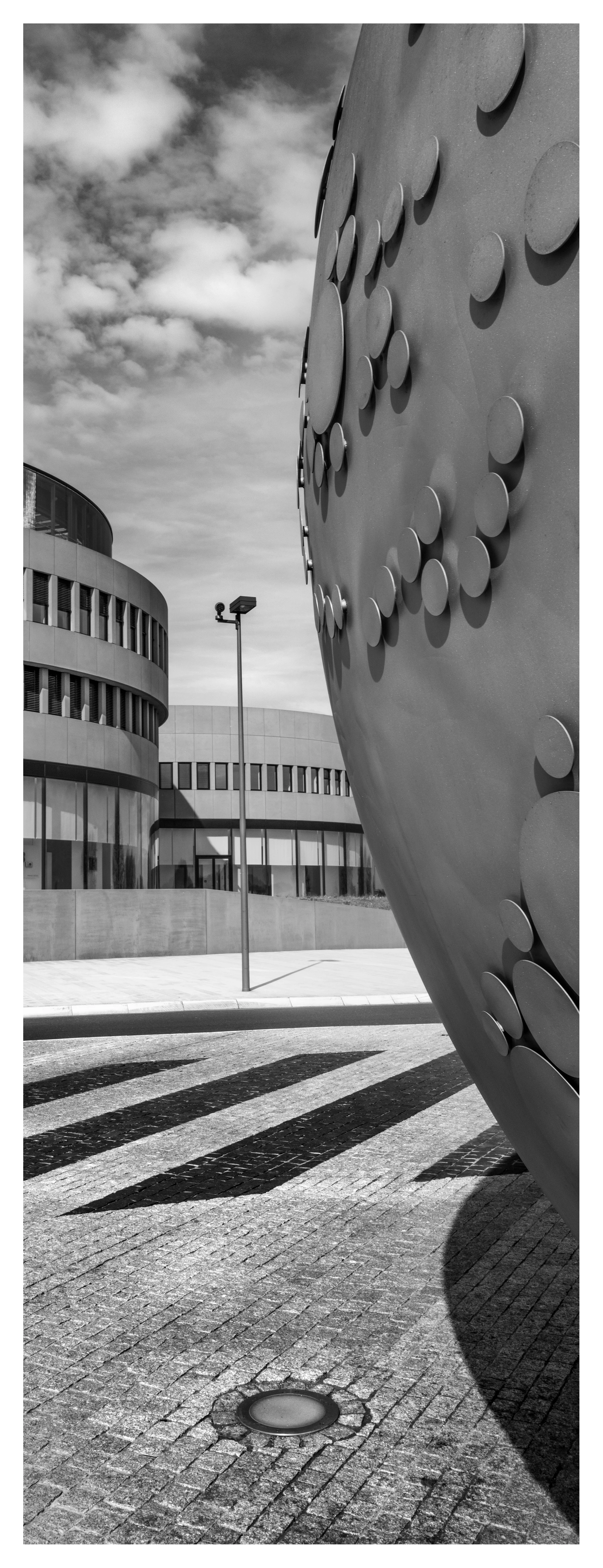 黑白照片:一座带有凸起陀螺元素的大型圆形雕塑矗立在Leitz-Park弯曲的主楼和铺砌广场前。