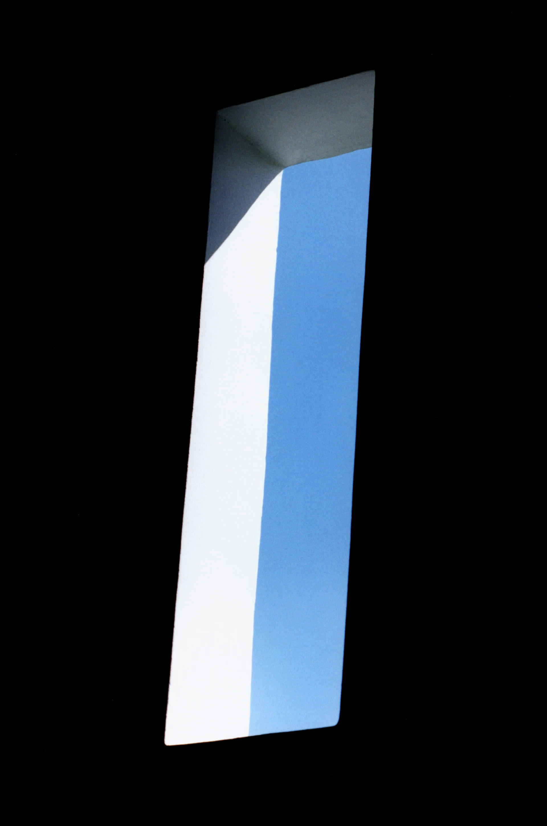 Minimalistischer Blick auf den blauem Himmel, aus dem Schatten eines Raumes heraus durch ein schmales Fensterloch.