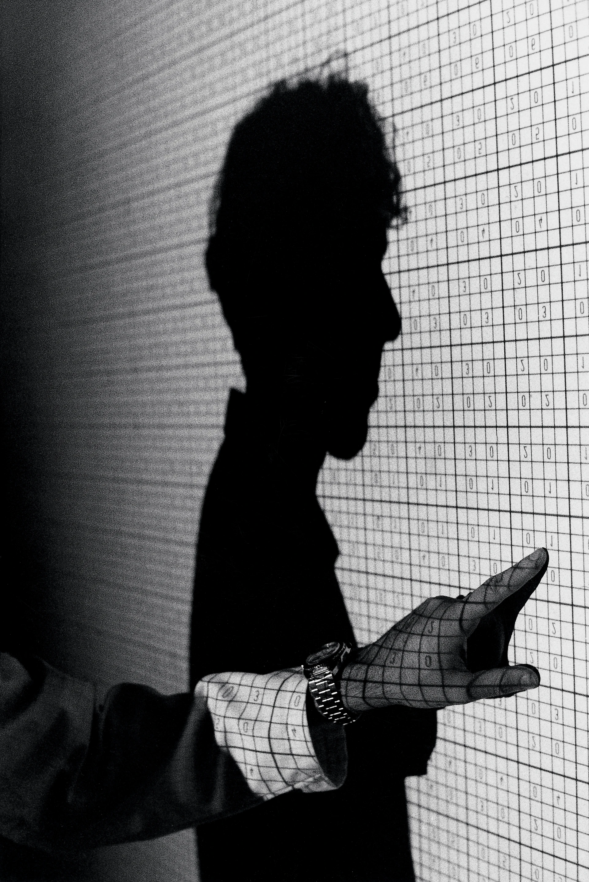 Schwarz-Weiß-Bild eines Mannes der auf eine Testbildwand zeigt, wobei man den Kopf nur als Schatten sieht.