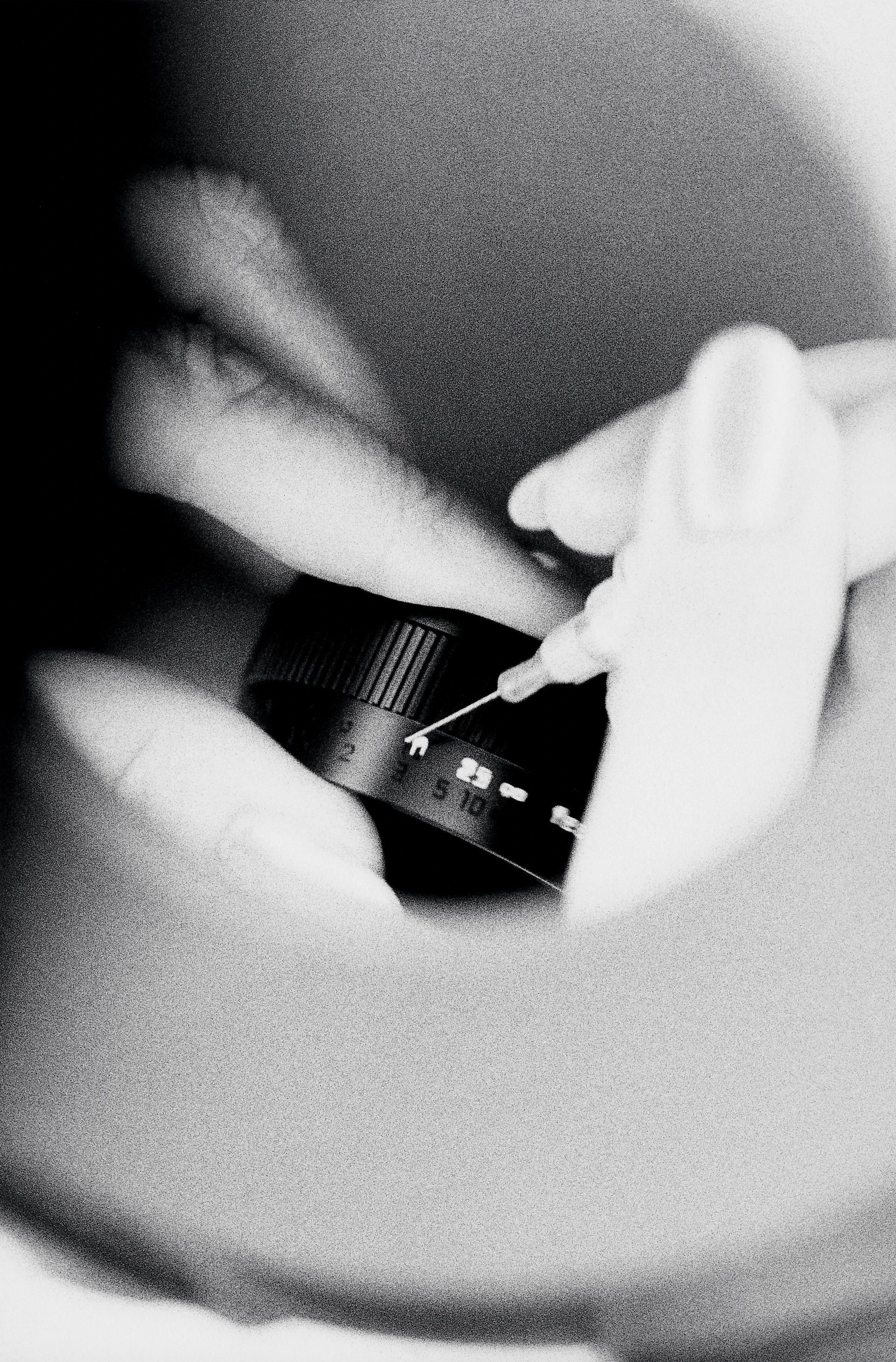 Primo piano in bianco e nero di mani intente a colorare con un ago i numeri di un obiettivo.