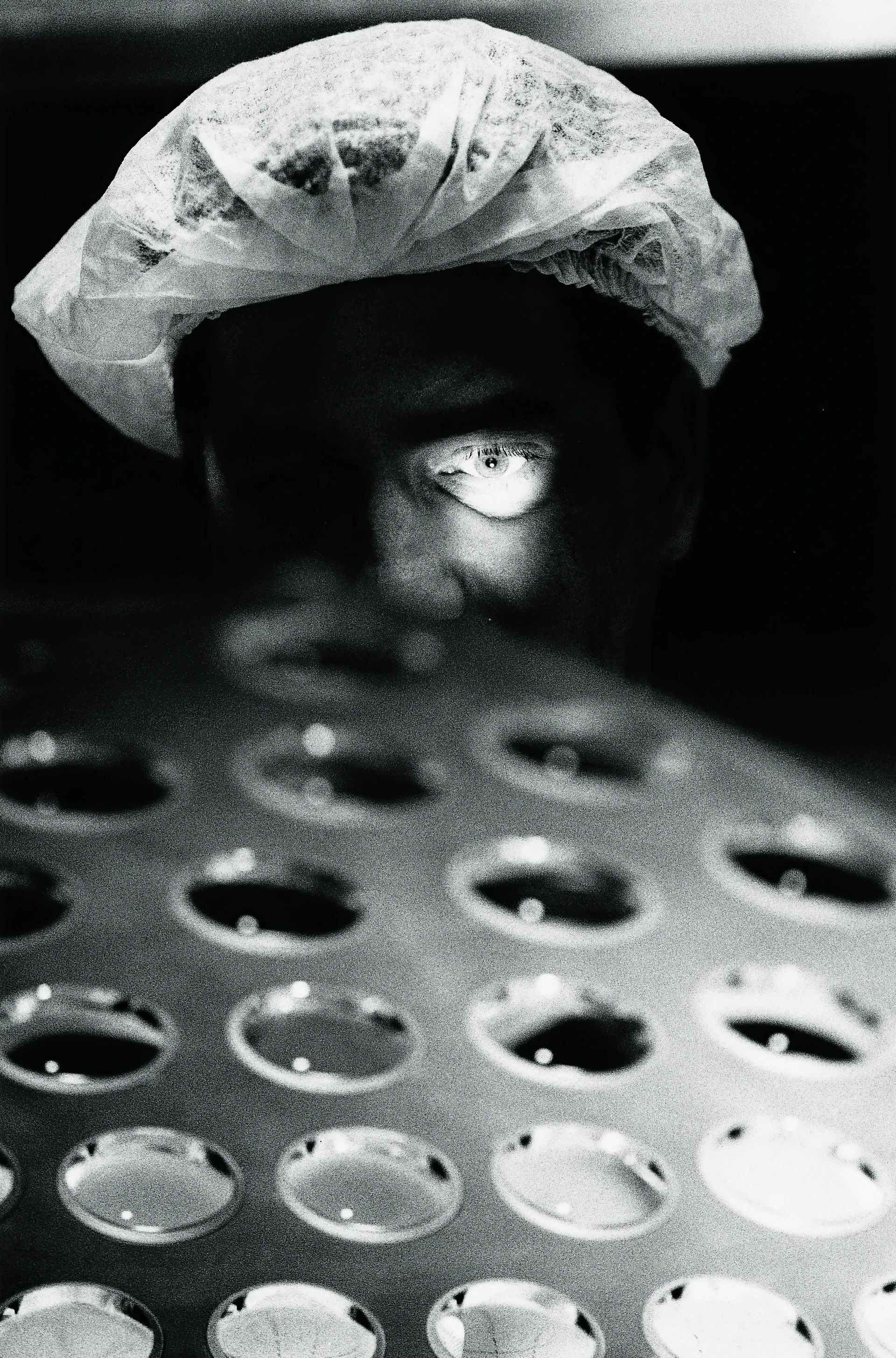 Emozionante foto in bianco e nero di un operatore di laboratorio di cui è illuminato l’occhio, intento a eseguire un controllo visivo di una palette di lenti per obiettivi.