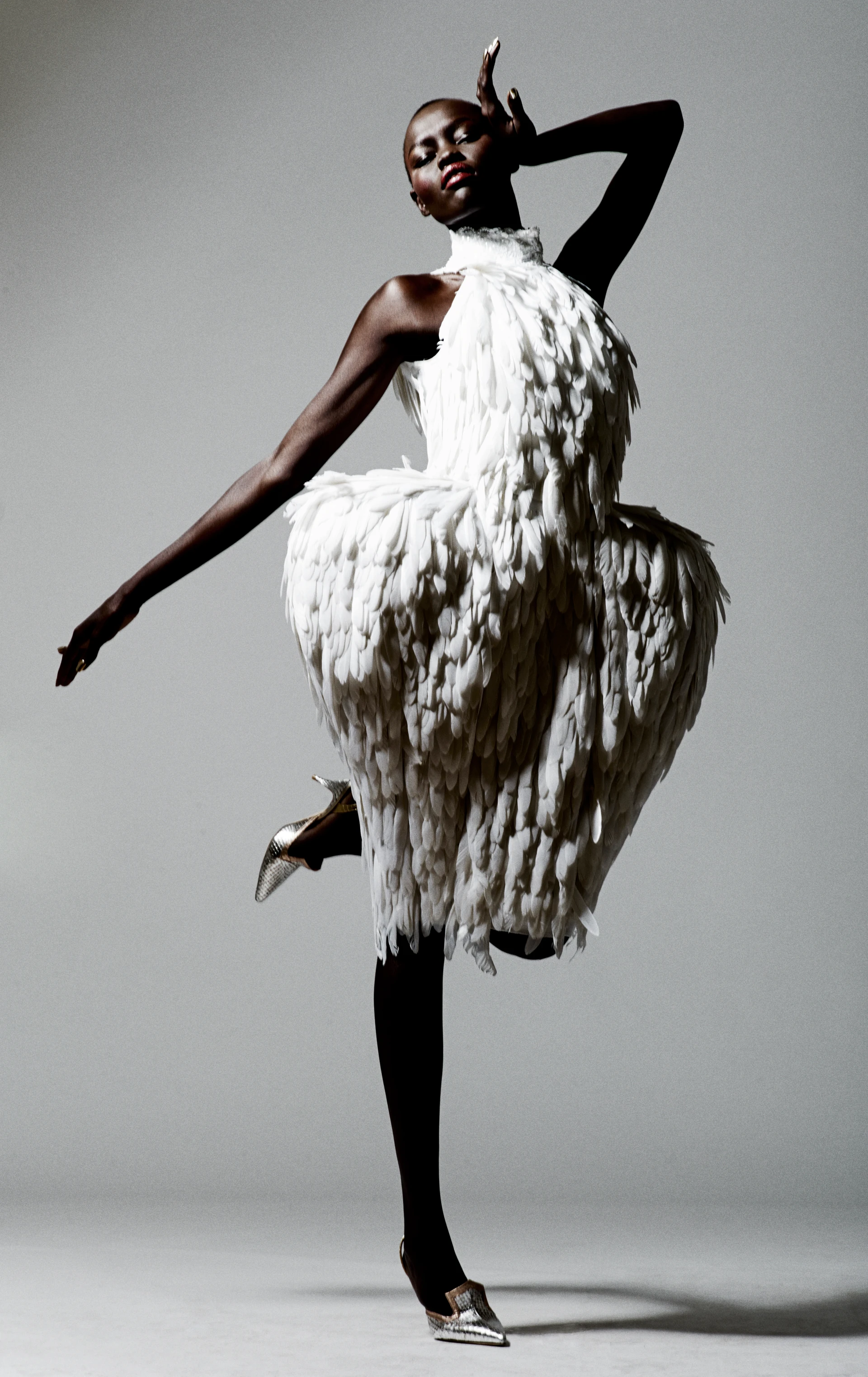 Studioaufnahme einer Schwarzen Dame, die in weißem Federkleid in dramatischer Geste posiert.