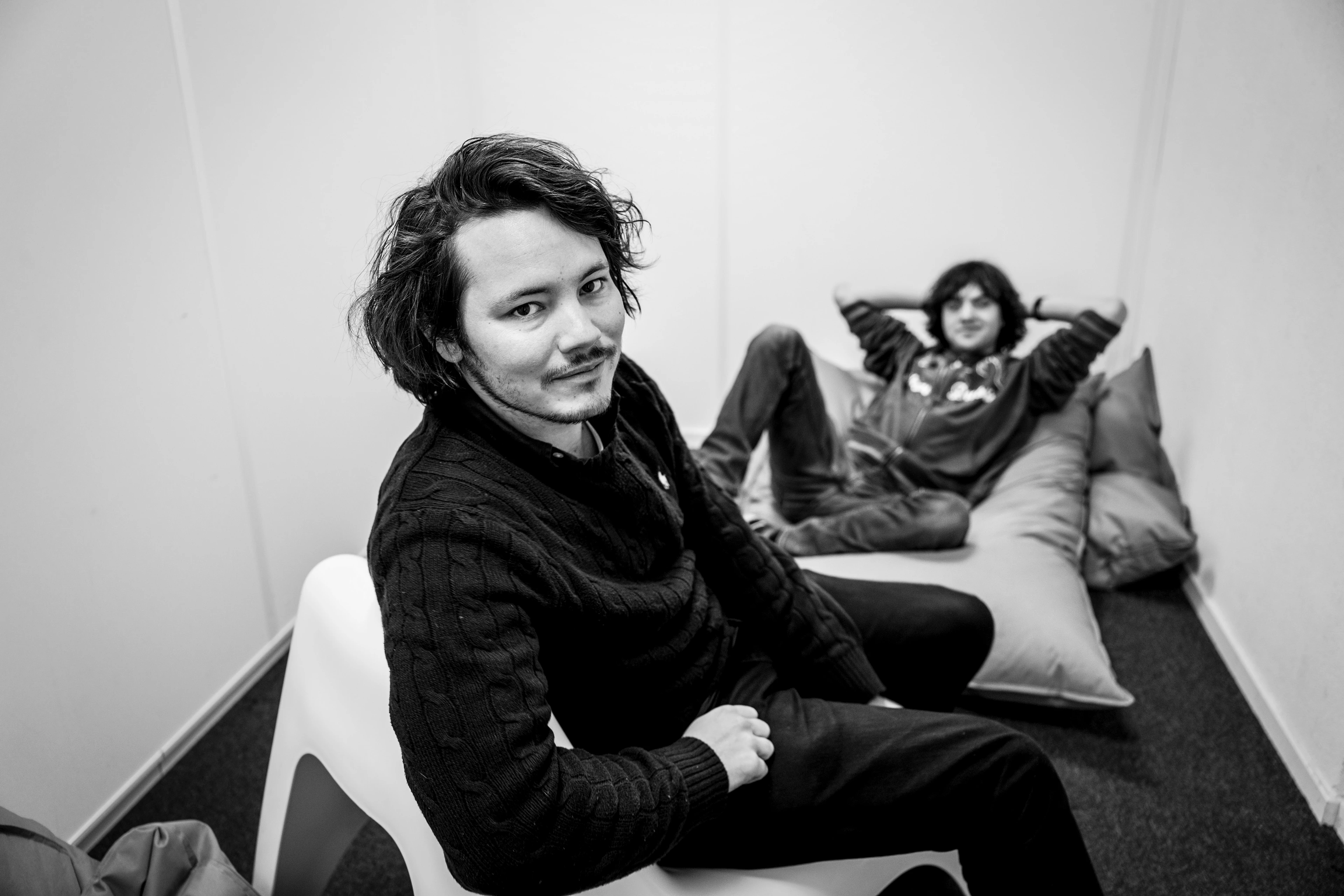 Boyan Slat sits relaxed on a beanbag in a small meeting room while another person sits on a chair in front of him, smiling at the camera.