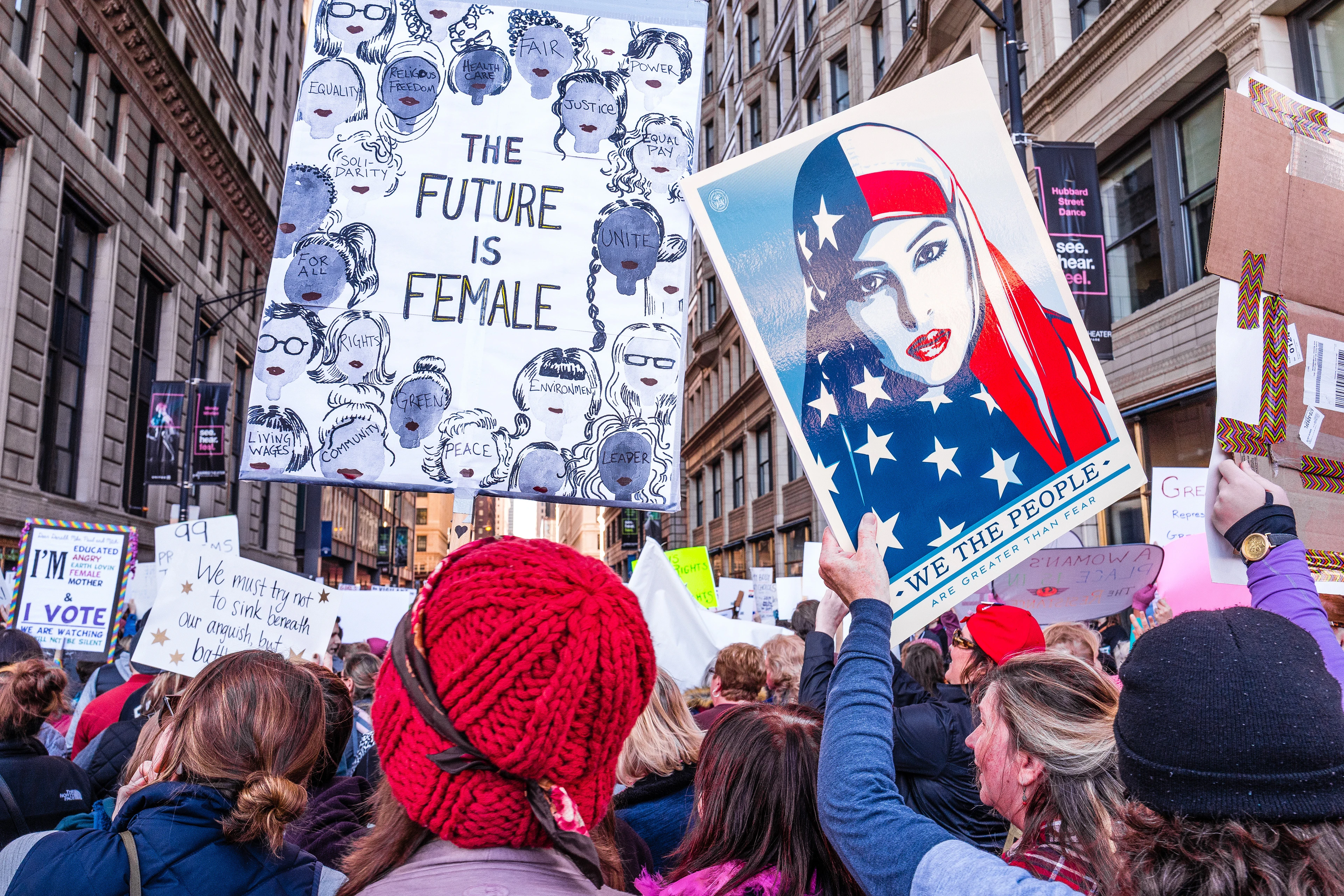 In New York, women stand crowded together on a street holding up signs, including a large portrait and a poster reading ‘The Future Is Female’, all looking in the same direction.