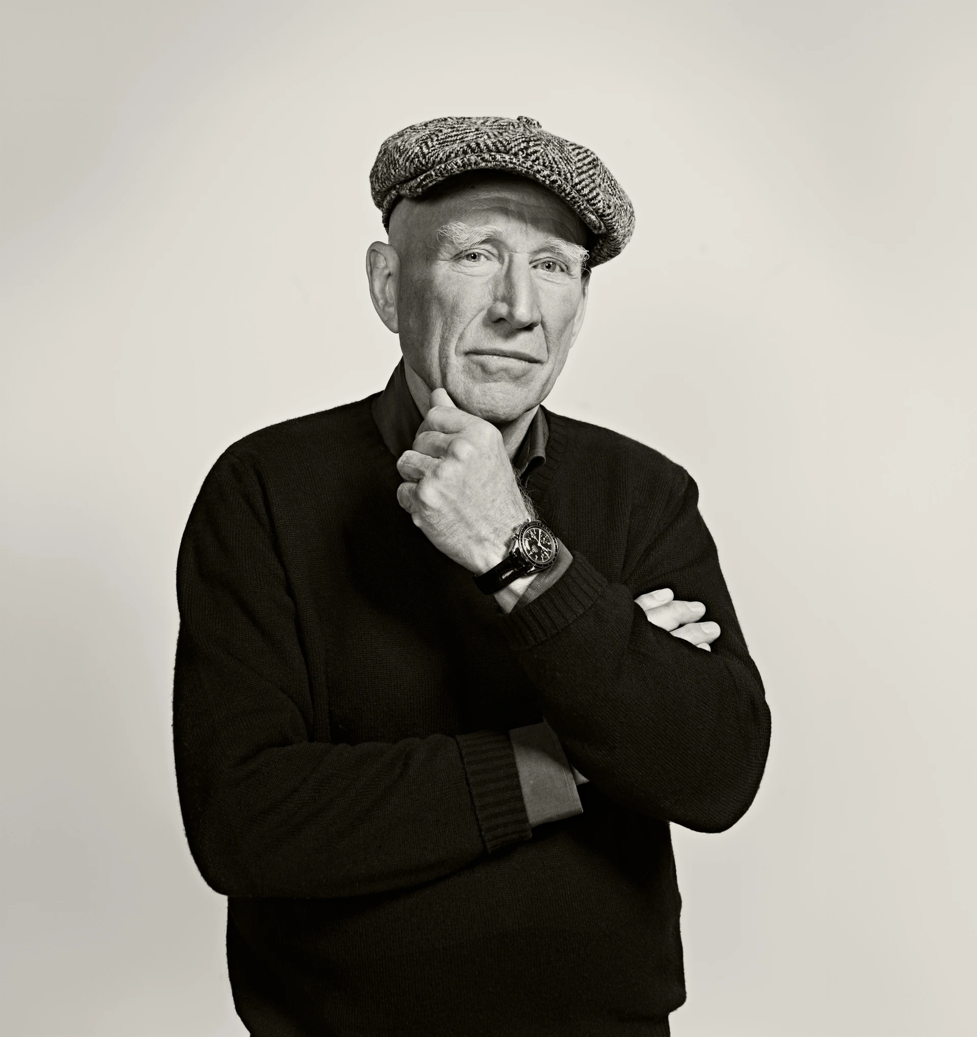 Black and white portrait of Sebastião Salgado, posing thoughtfully for the camera with a beret on his head and his arms folded.