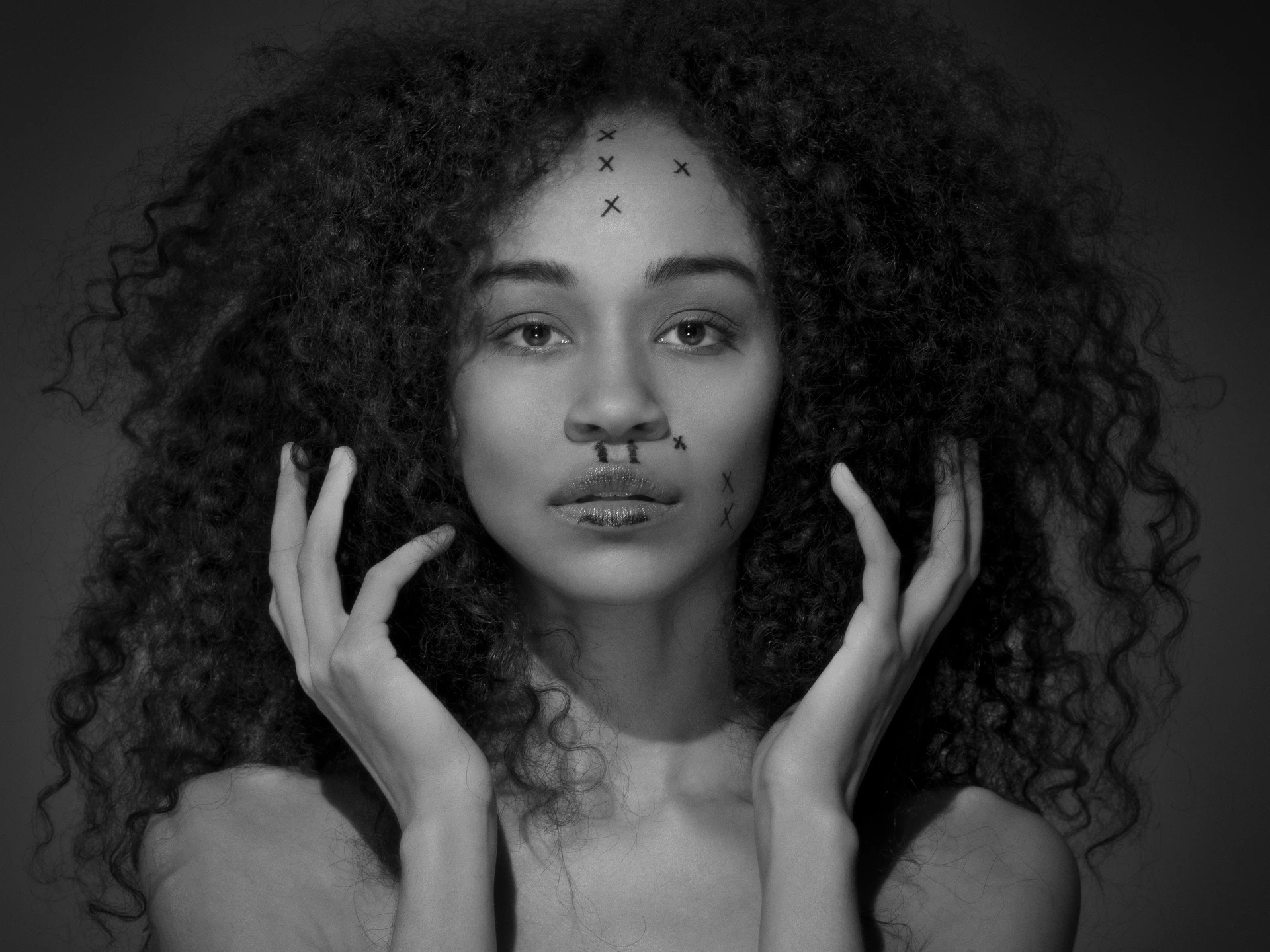 黑白肖像:一位靓丽女子的头部和裸露的肩膀,她双手轻托着丰盈的黑色卷发,微微张嘴望向相机镜头,摄影棚的灯光凸显出她鼻子、嘴唇、上唇和额头上的各种手术痕迹。