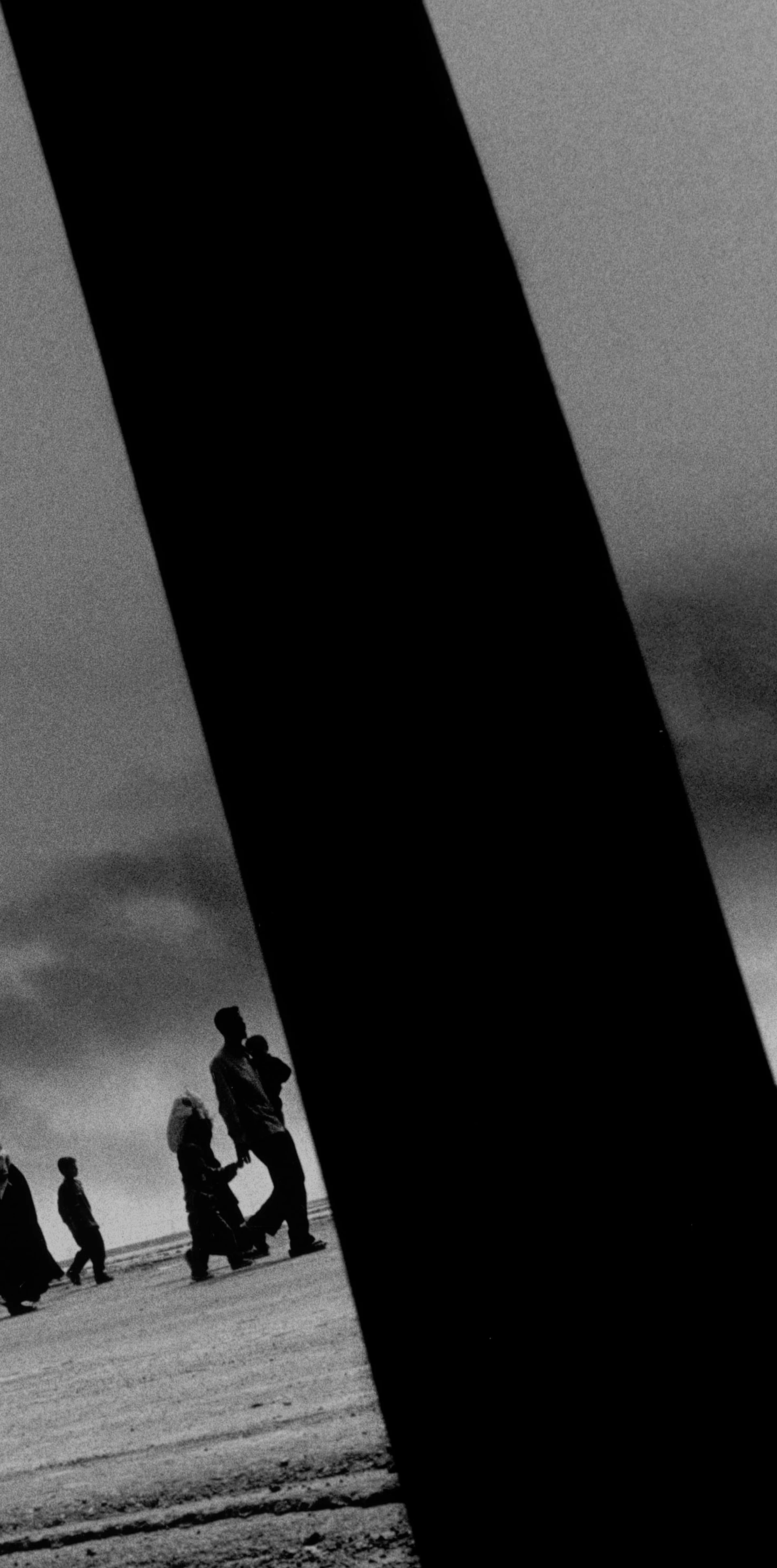 Photographie dramatique en noir et blanc d’un garçon au regard fixe photographié à travers un trou dans une épave de char, les restes d’un hélicoptère se trouvent à l’arrière-plan.