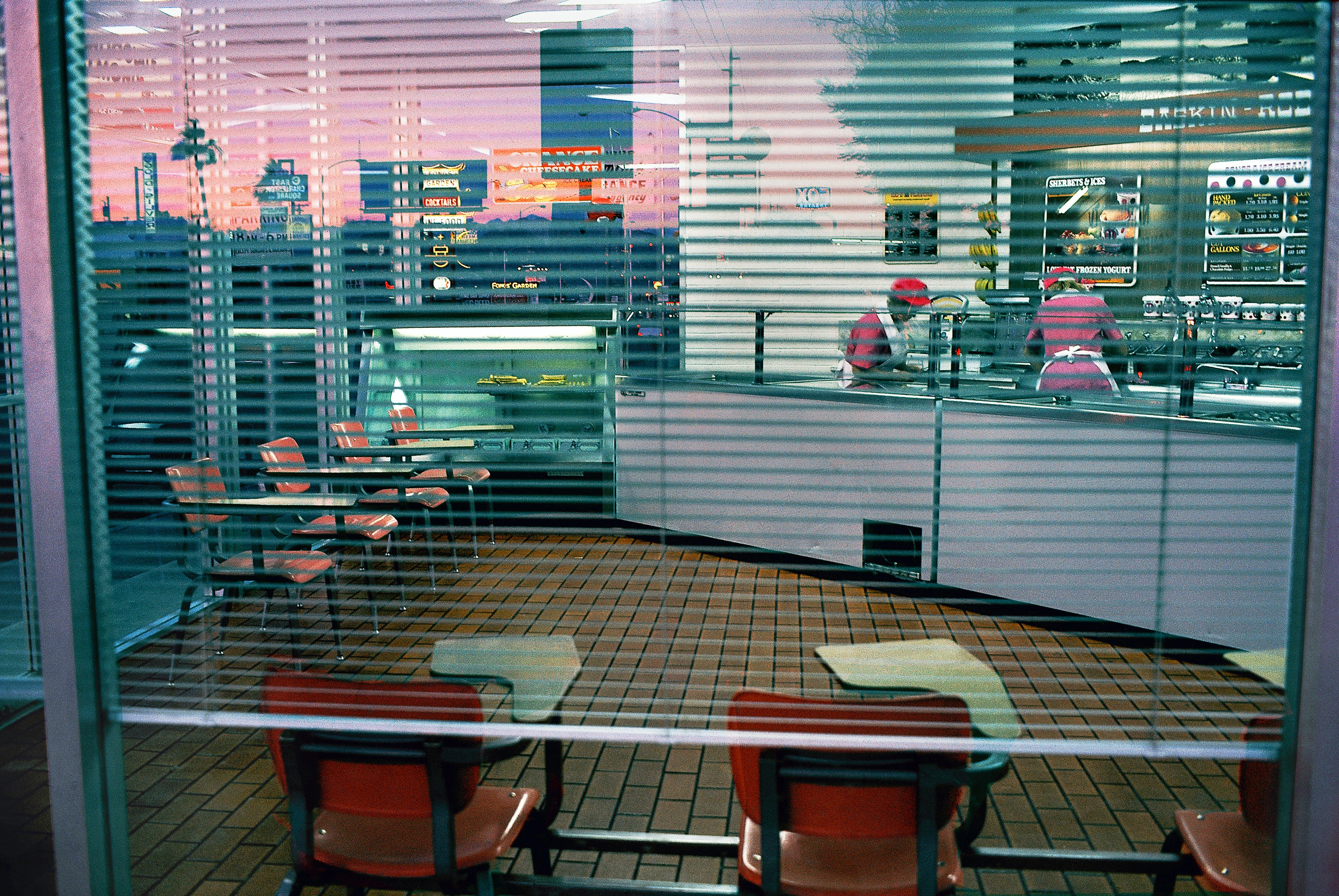 アイスクリームカフェの窓越しに2人のスタッフの姿が見え、窓にはピンク色に染まった夕焼け空が映り込んでいる。